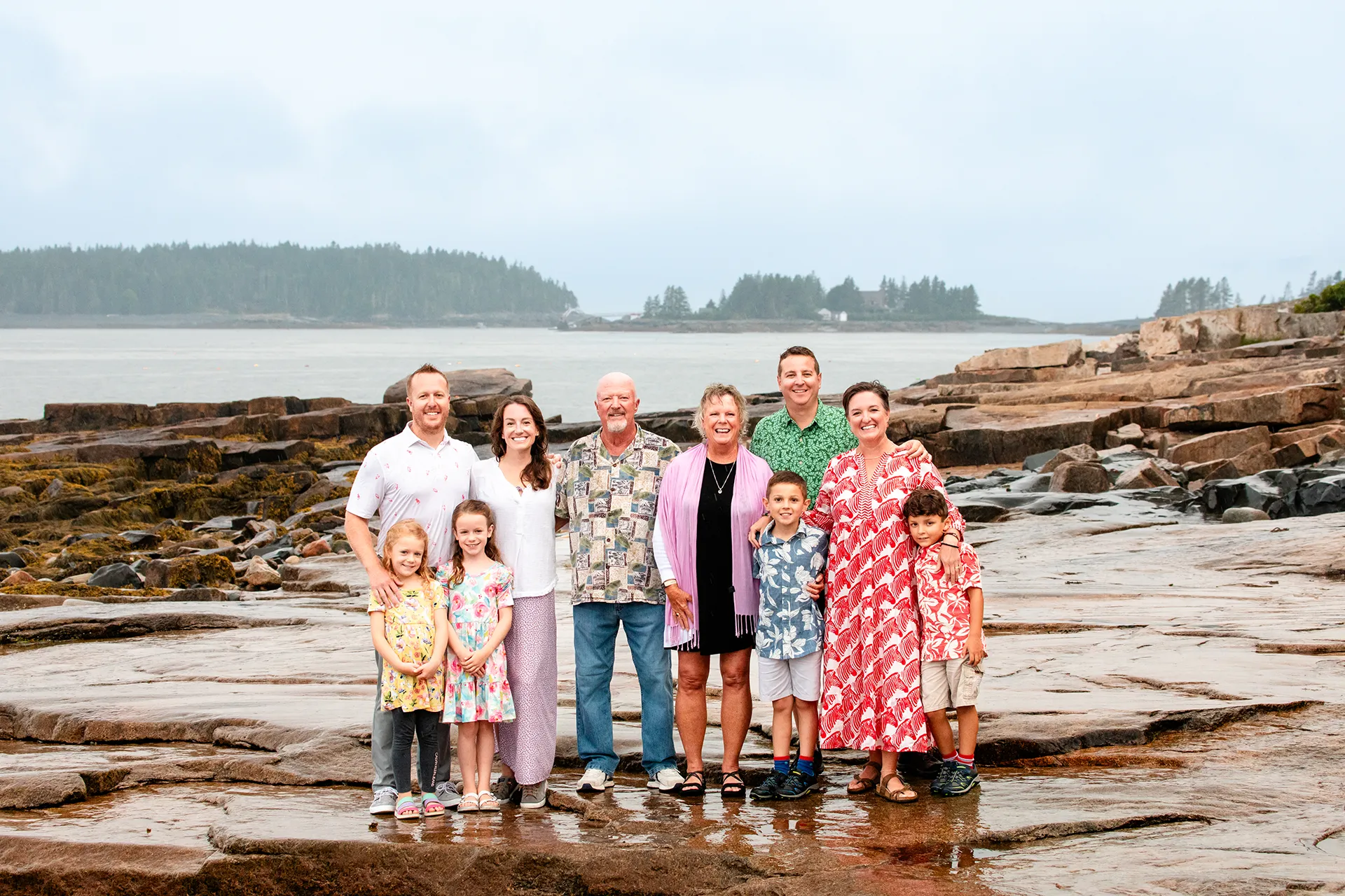 An extend family pose in front of a foggy harbor at Grindstone Point in Winter Harbor, Maine during a family portrait session.