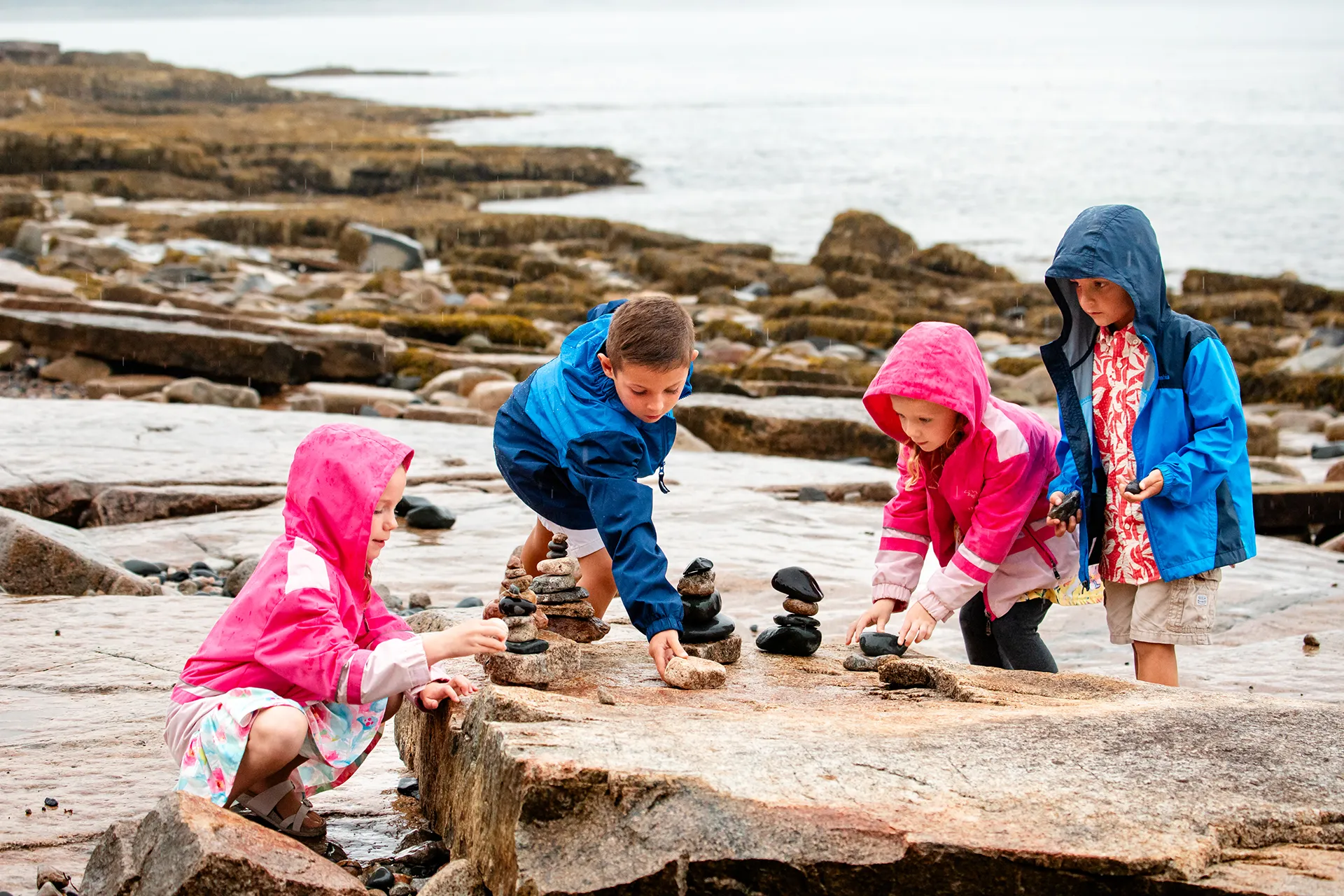 Children wearing rain play in the rain during a family portrait session Grindstone Point in Winter Harbor, Maine.