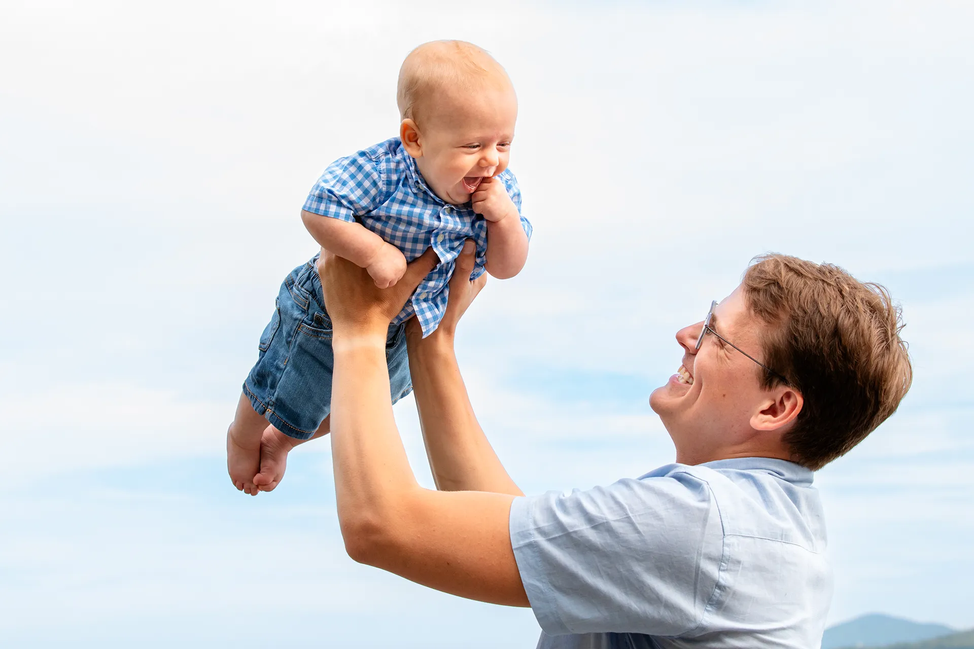 maine family photography moldawer mandsager 06 A dad lifts a young boy in the air as he smiles during a family portrait session in Lamoine, Maine.