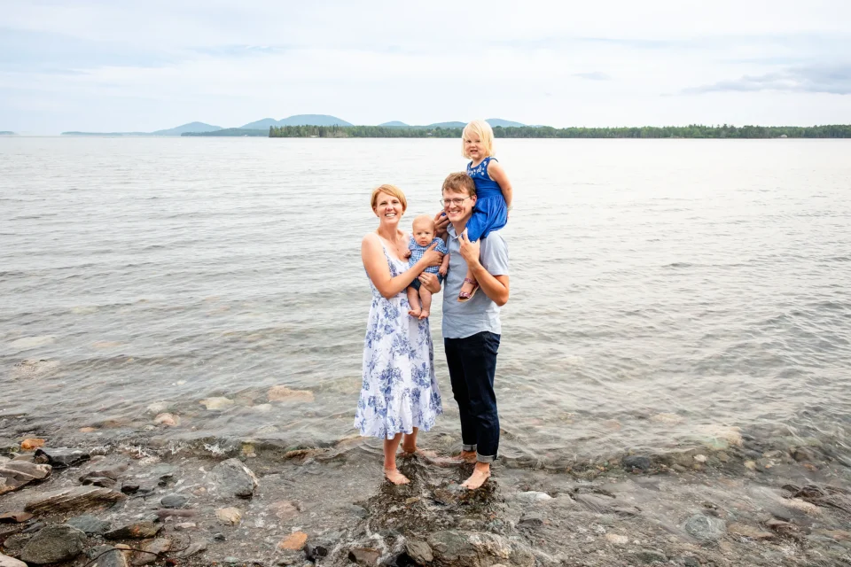 A mom and dad stand in the ocean and pose with two young children during a family portrait session in Lamoine, Maine.