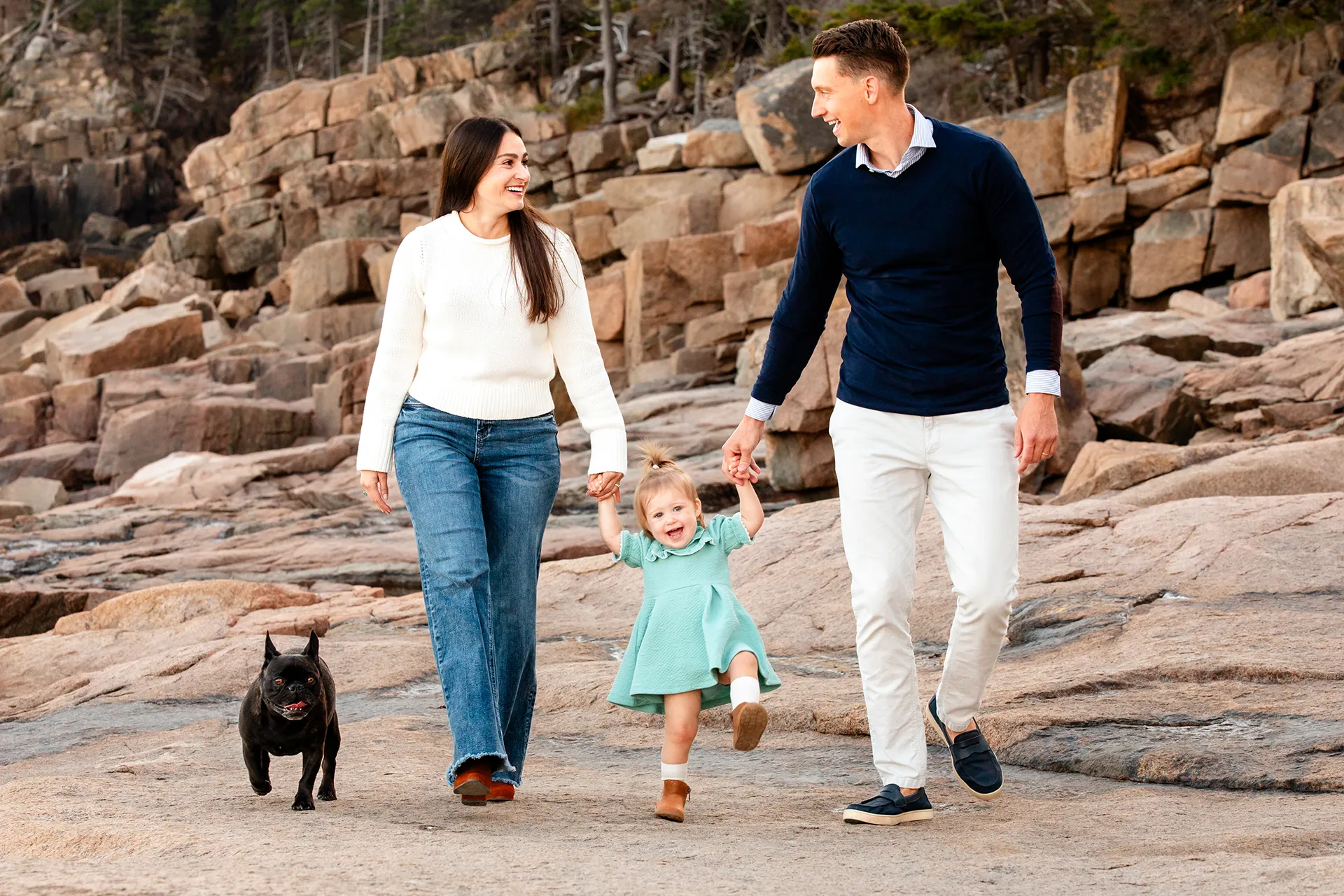 maine family photography myer 12 Two young parents walk along a rocky shore with their toddler and dog in near the Ocean Path Trail in Acadia National Park, Maine.
