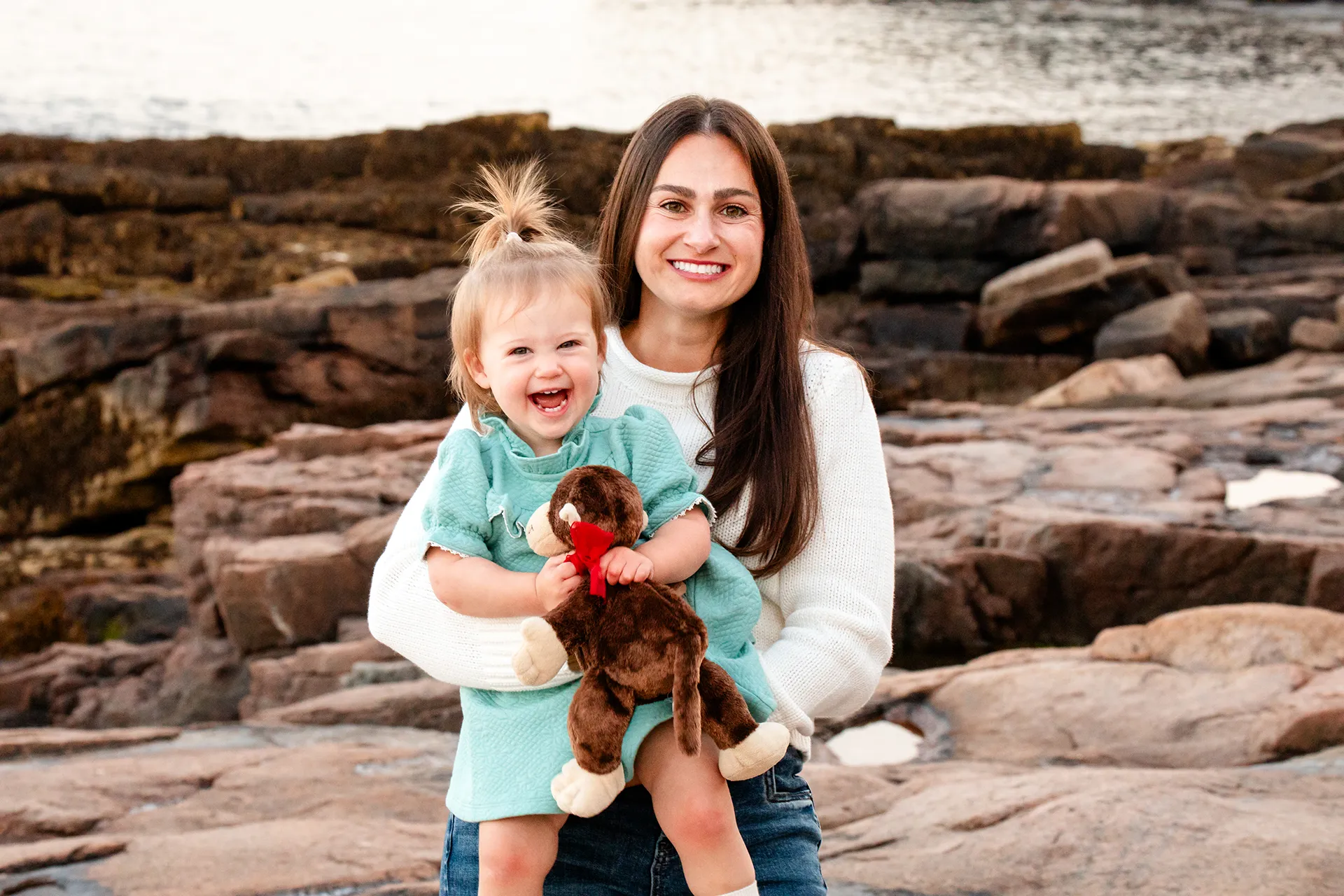 maine family photography myer 13 A mom holds her daughter as she smiles and poses during a family portrait session near the Ocean Path Trail in Acadia National Park.