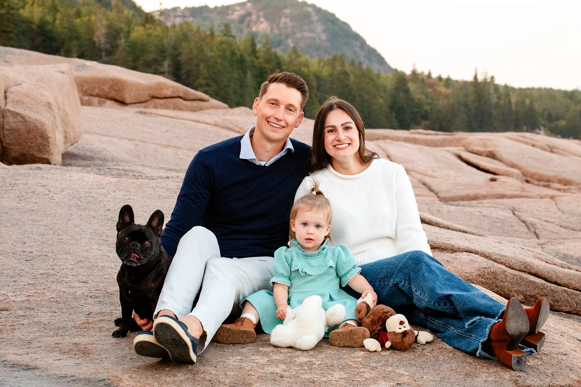 maine family photography myer 15 A mom and dad sit and pose with their daughter and dog during a family portrait session near the Ocean Path Trail in Acadia National Park.