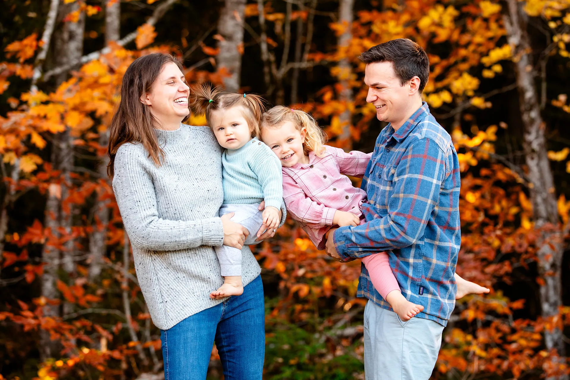 maine family photography sleeper wolland 03 A mother and father hold their young daughters as they laugh during a fall family portrait session near Bangor, Maine.