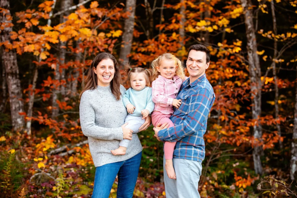 A mother and father hold their young daughters during a fall family portrait session near Bangor, Maine.