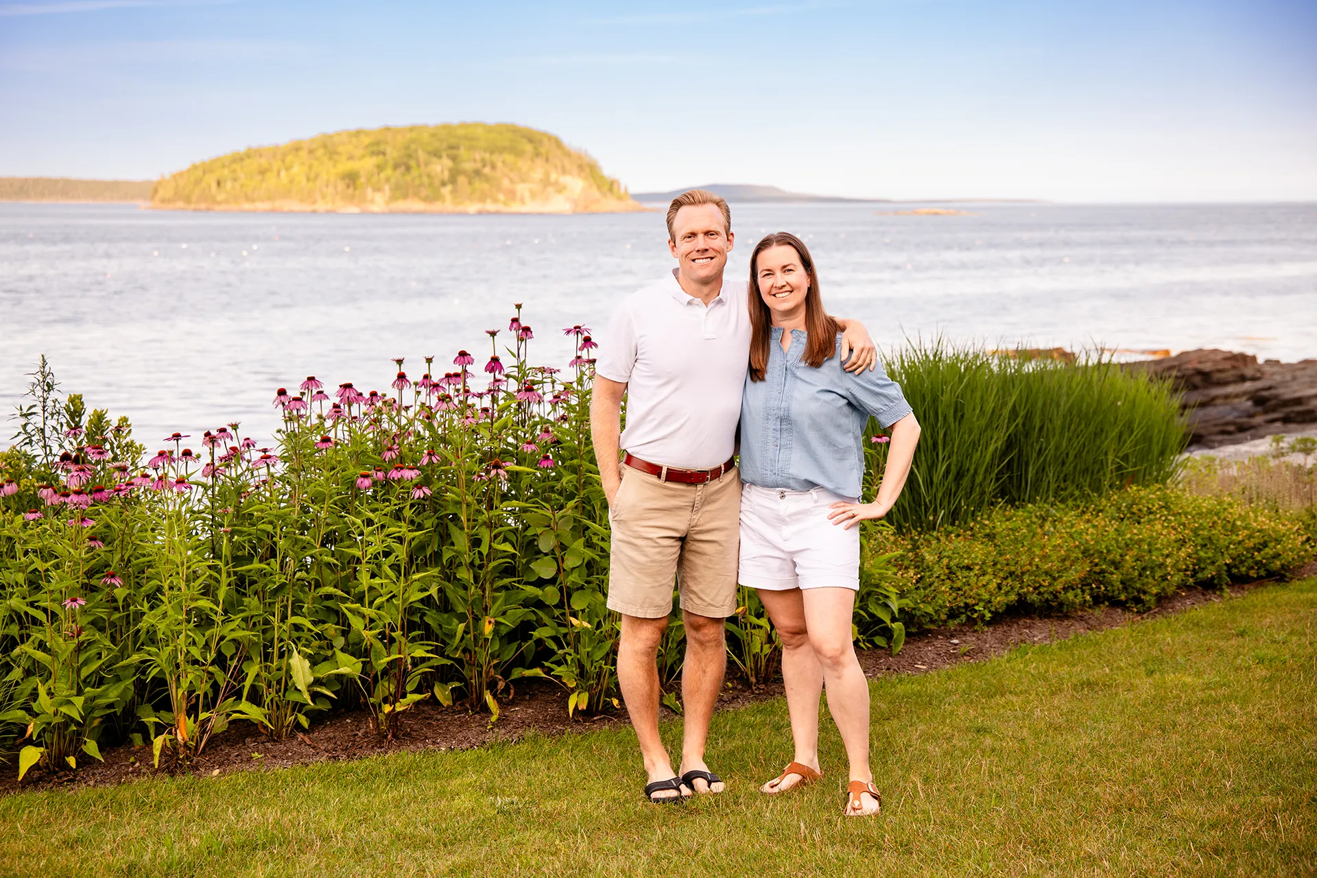A man and woman smile and pose during a portrait session in front of Frenchman Bay at the Bar Harbor Inn & Spa in Bar Harbor, Maine.
