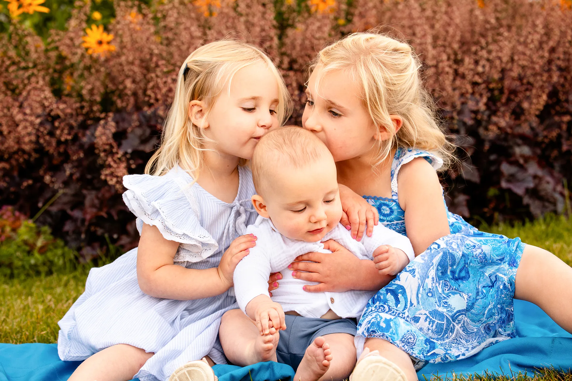 Two young girls kiss a baby on the head during a portrait session at the Bar Harbor Inn & Spa in Bar Harbor, Maine.