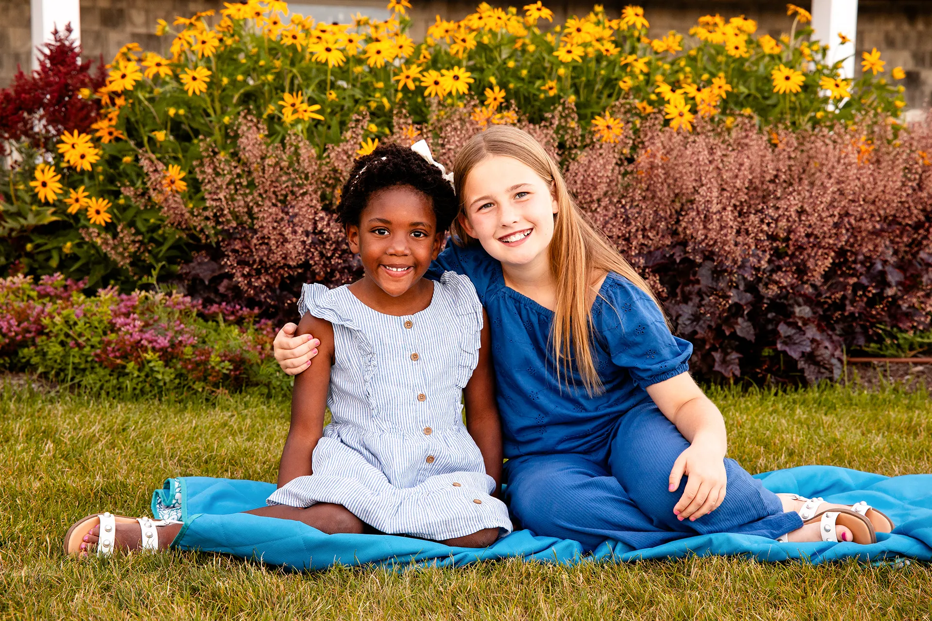 Two young girls sit on a blanket in the grass and smile during a portrait session at the Bar Harbor Inn & Spa in Bar Harbor, Maine.