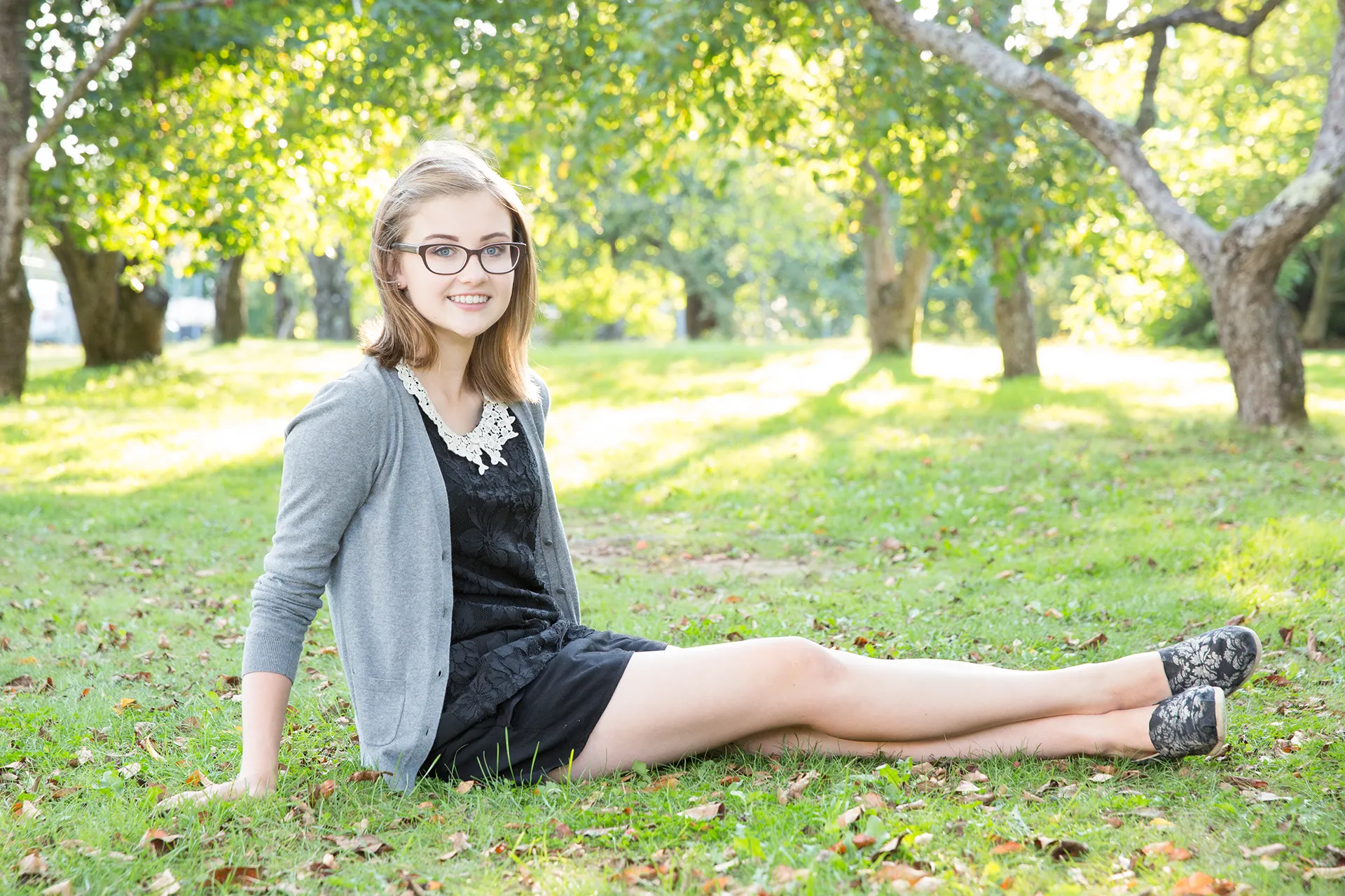 maine portrait photography emma 07 A girl sits in the grass and smiles during a senior portrait session in Littlefield Ornamental Garden at the University of Maine in Orono.