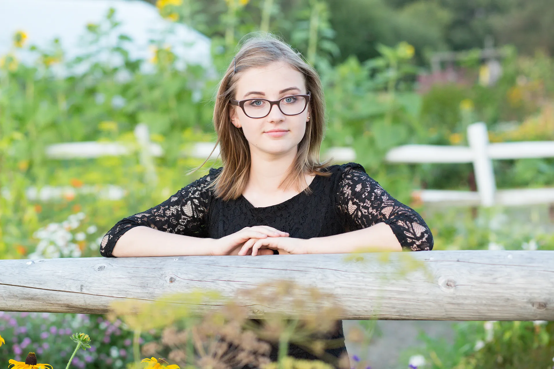 maine portrait photography emma 16 A girl rests her hands on a fence while posing in a garden during a senior portrait session at Rogers Farmer near the University of Maine in Orono.