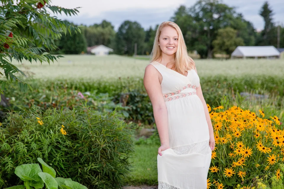 A high school senior smiles and poses in a garden at the Rogers Farm in Old Town, Maine near the University of Maine.