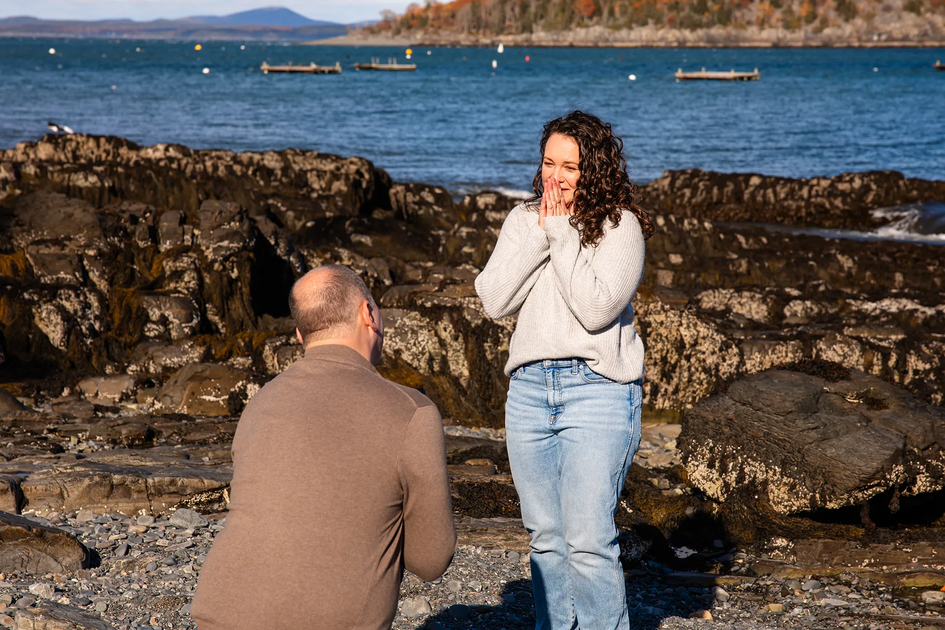 A woman covers her face while a man kneels in front of her during a marriage proposal at the Bar Harbor Inn and Spa near Acadia National Park.