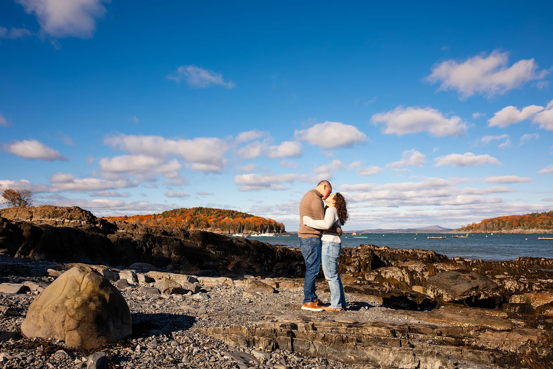 A man and woman kiss on a rocky beach during a marriage proposal at the Bar Harbor Inn and Spa near Acadia National Park.