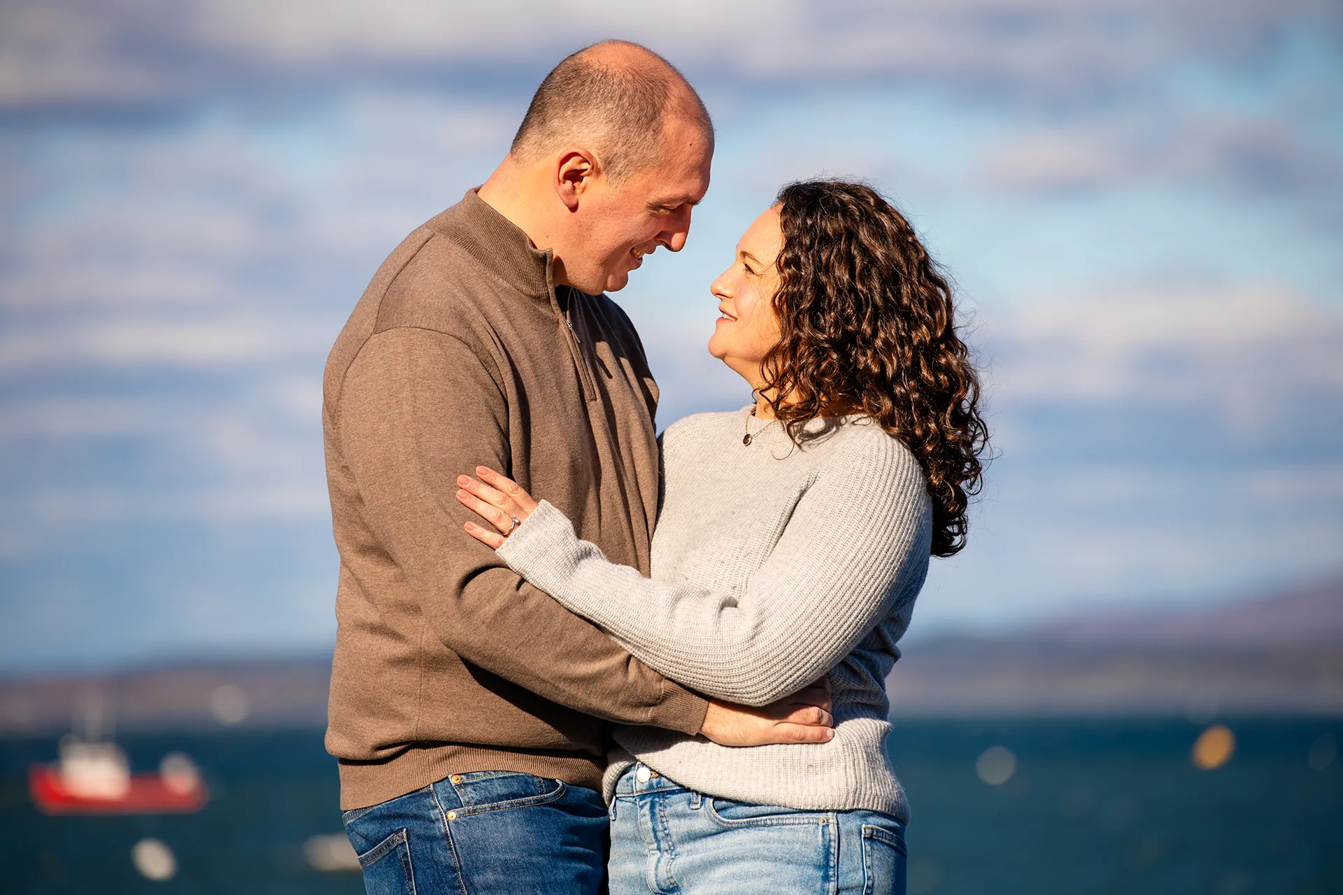 A newly engaged couple smile at each other while posing in front of Frenchmans Bay at the Bar Harbor Inn and Spa in Maine.