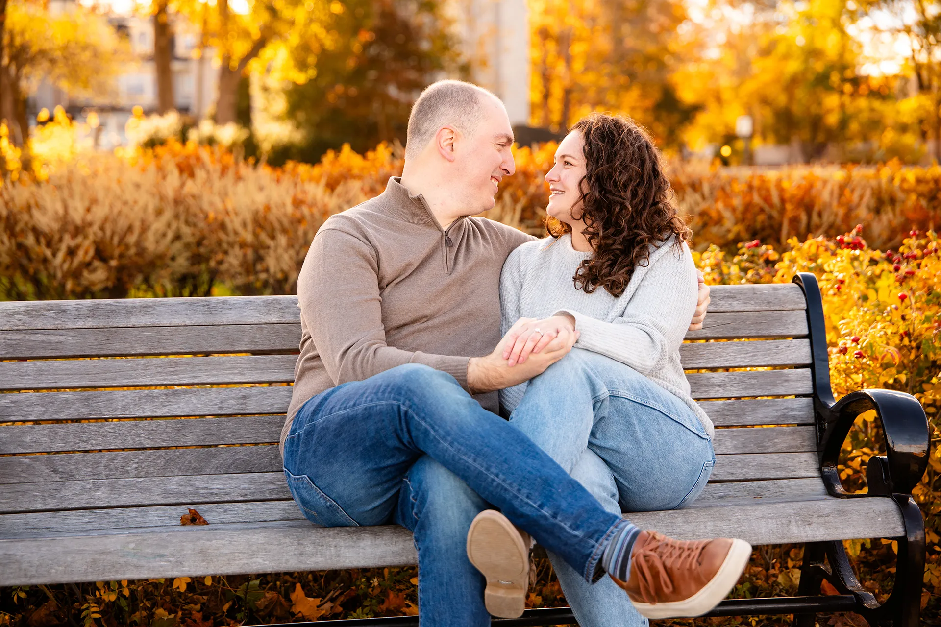 A recently engaged couple hold hands and sit on a bench during engagement portraits at the Bar Harbor Inn and Spa near Acadia National Park.
