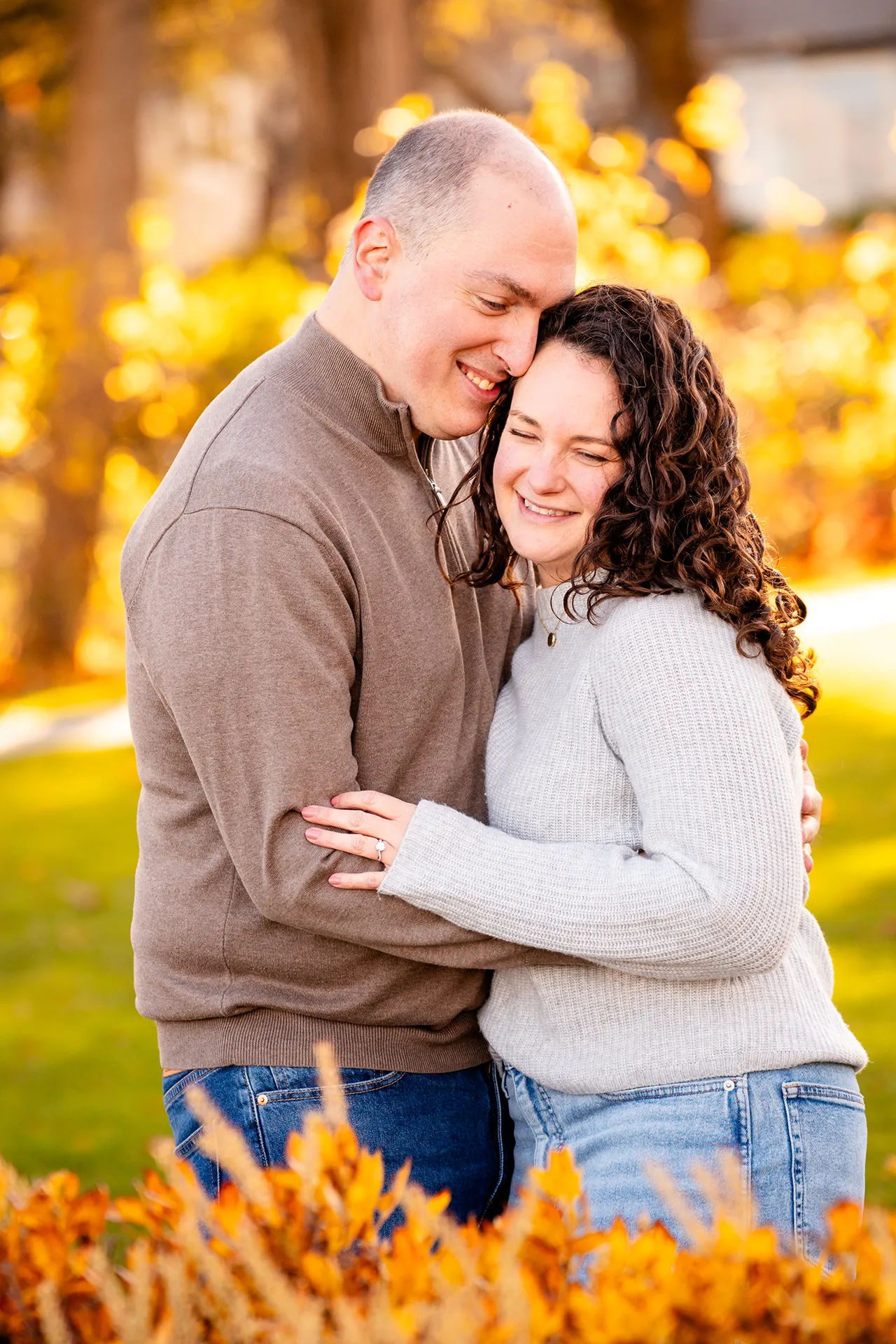 A man and woman smile as they cuddle together during engagement portraits at the Bar Harbor Inn and Spa near Acadia National Park.