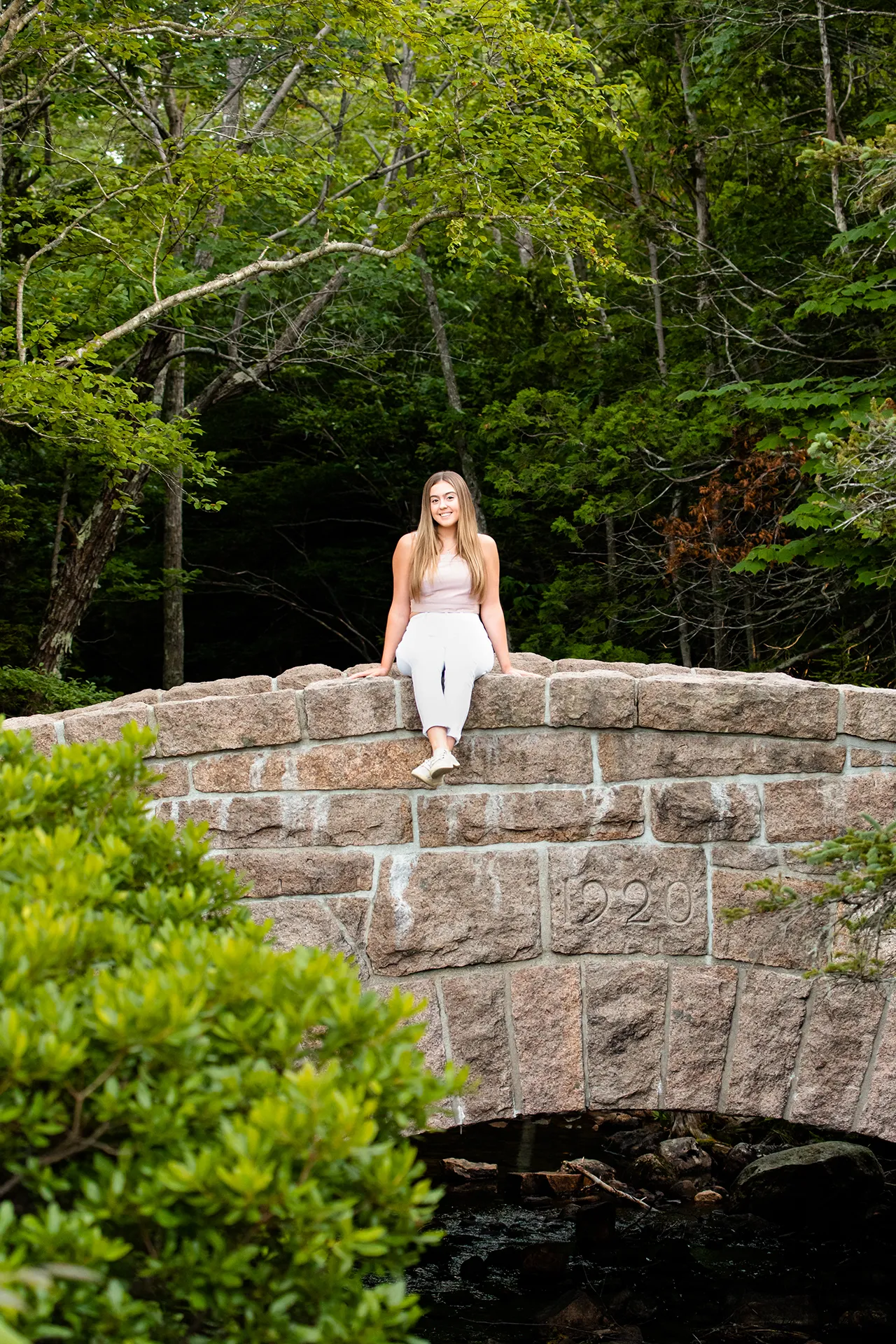 maine senior photography brooke 02 A girl smiles and sits on a stone bridge during a senior portrait session at Jordan Pond in Acadia National Park, Maine.