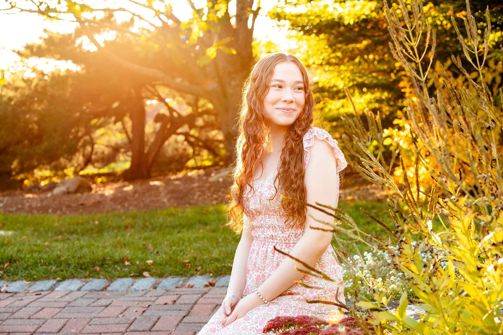 A girl sits and poses in the LIttlefield Ornamentals Garden during a senior portrait session at the University of Maine.
