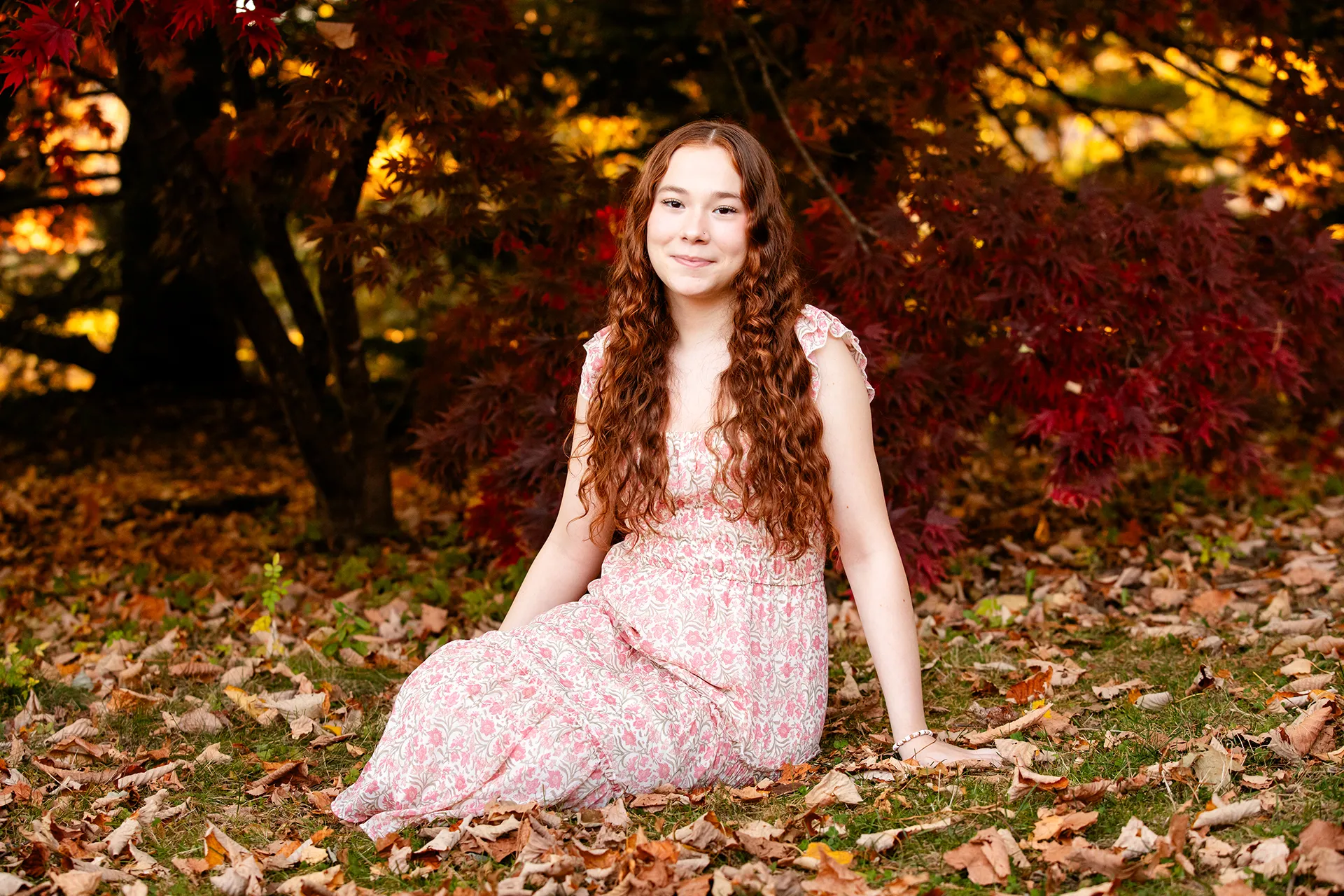 A high school senior sits in leaves during a portrait session at the LIttlefield Ornamentals Garden at the University of Maine.