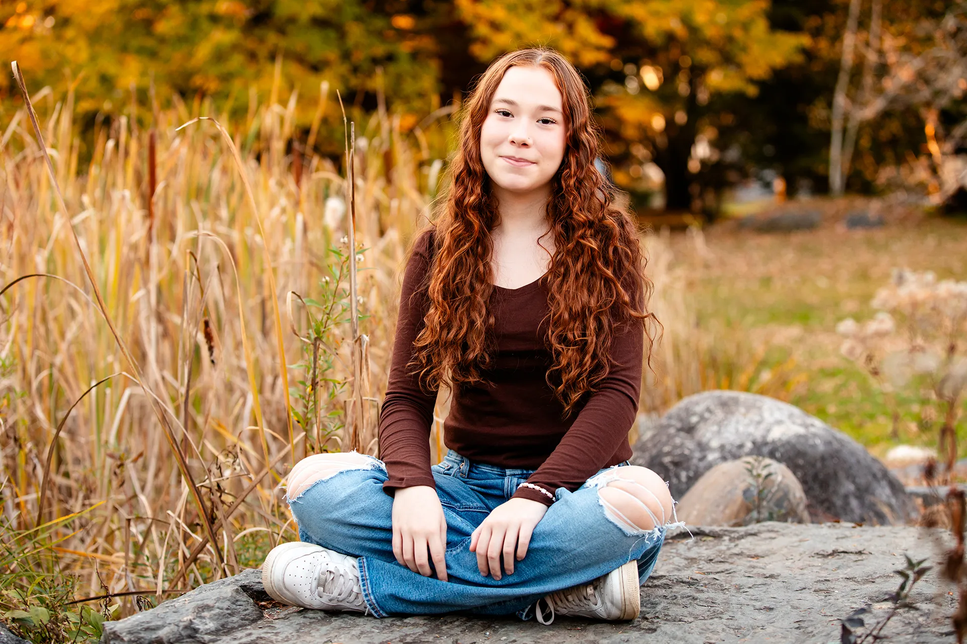 A high school senior sits amidst cat o' nine tails during a portrait session at LIttlefield Ornamentals Garden at the University of Maine.