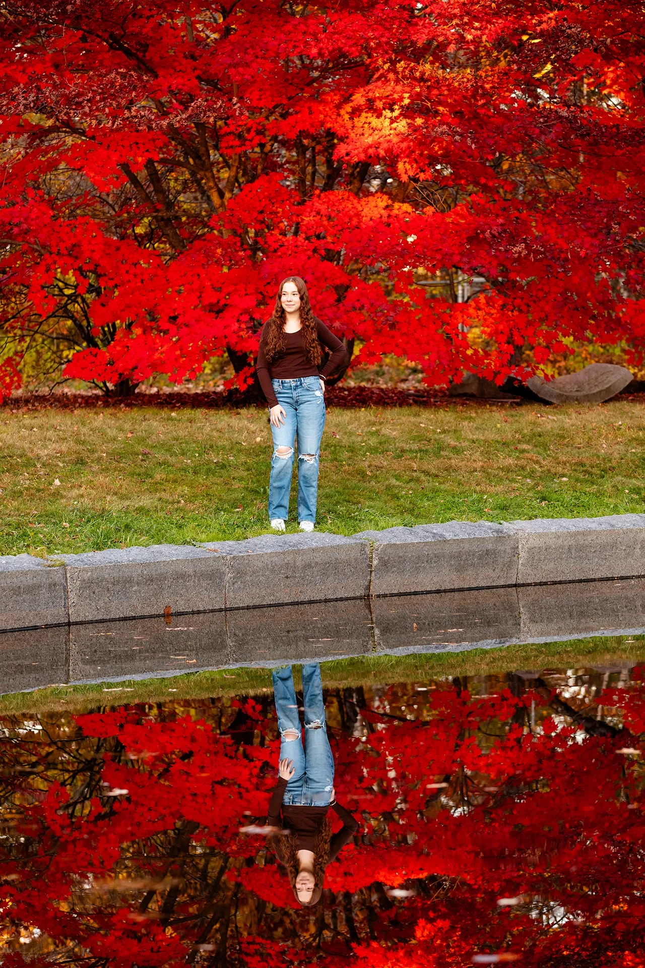 A high school senior poses in front of a red tree during a portrait session at the LIttlefield Ornamentals Garden at the University of Maine.