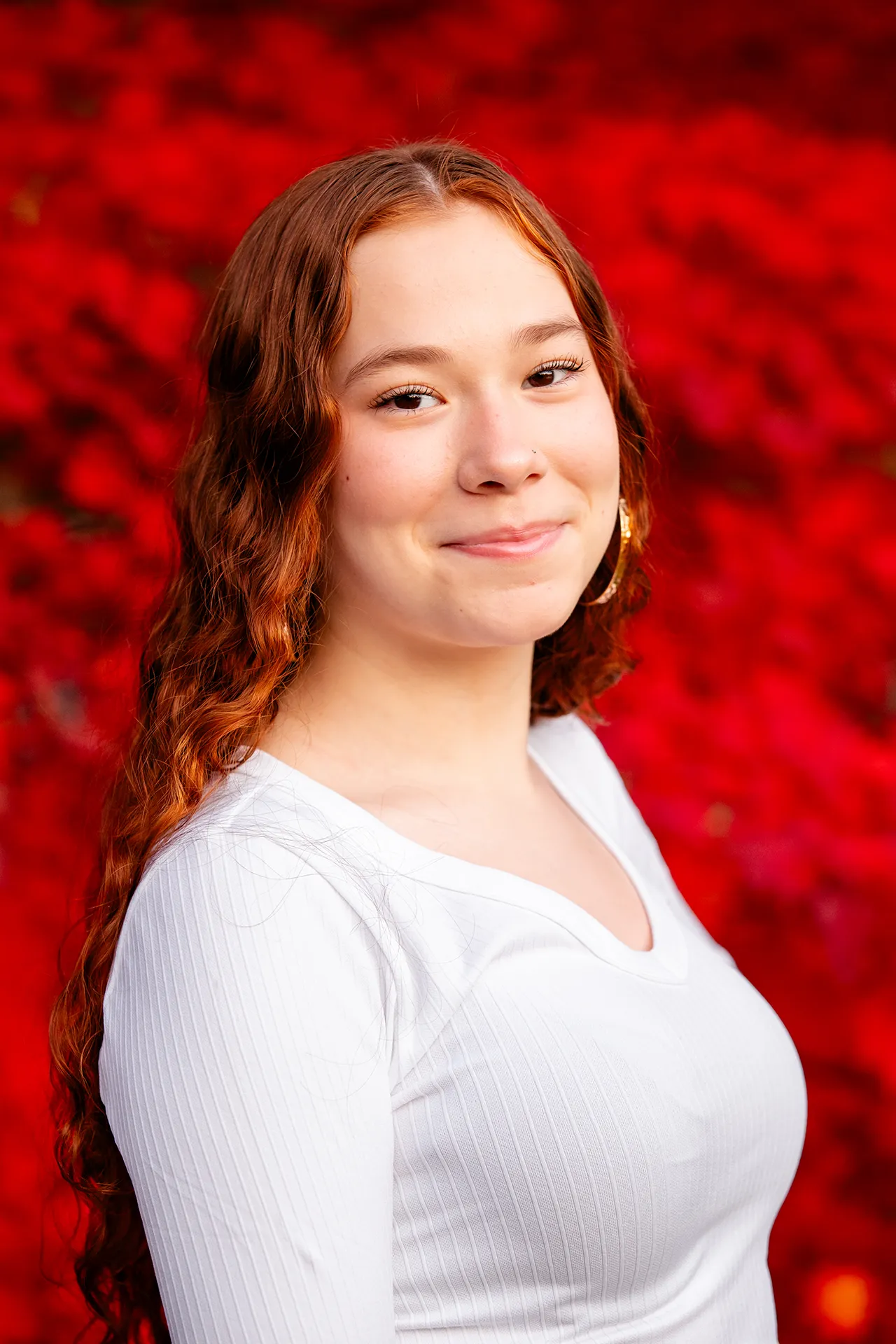 A high school senior poses in front of a red tree during a portrait session at the LIttlefield Ornamentals Garden at the University of Maine.