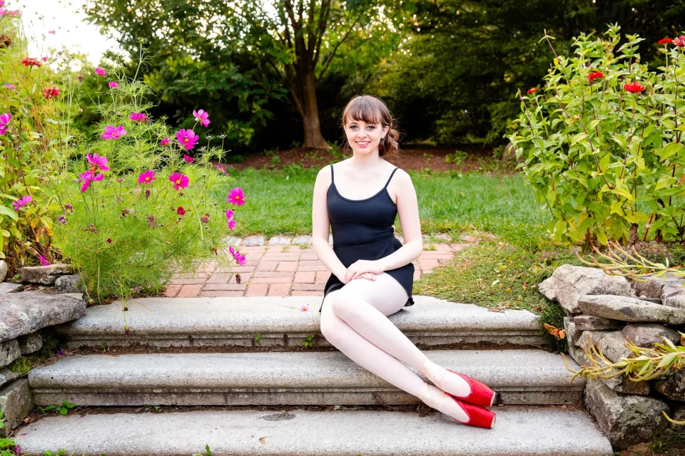 A girl wearing point shoes smiles and poses during senior portraits at the Littlefield Garden at the University of Maine in Orono.