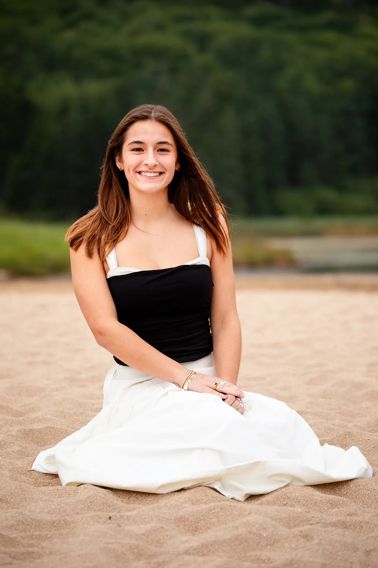 A high school senior sits and poses on Sand Beach during a senior portrait session in Acadia National Park.