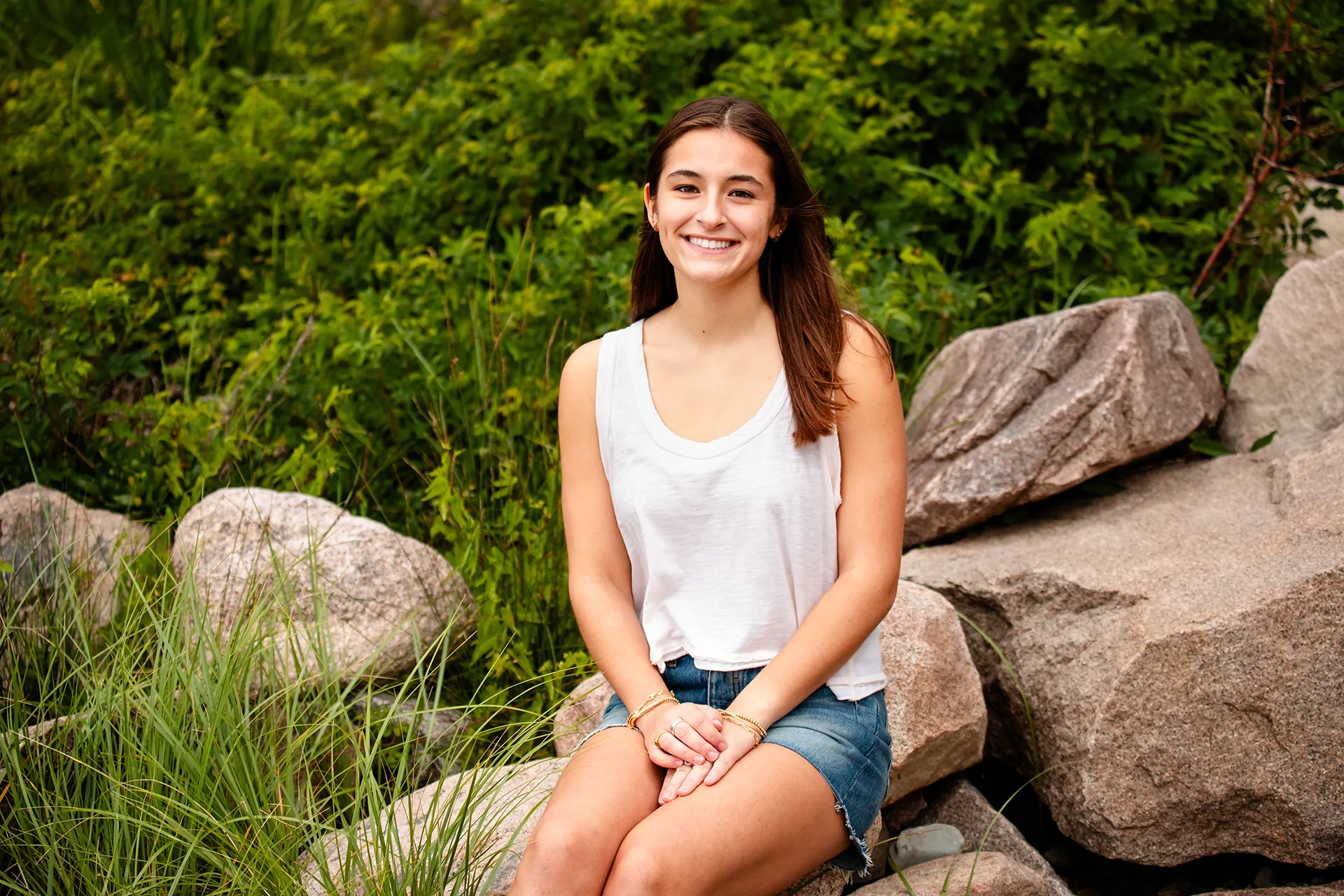 A girl sits and poses on a rock during a high school senior portrait session at Sand Beach in Acadia National Park.