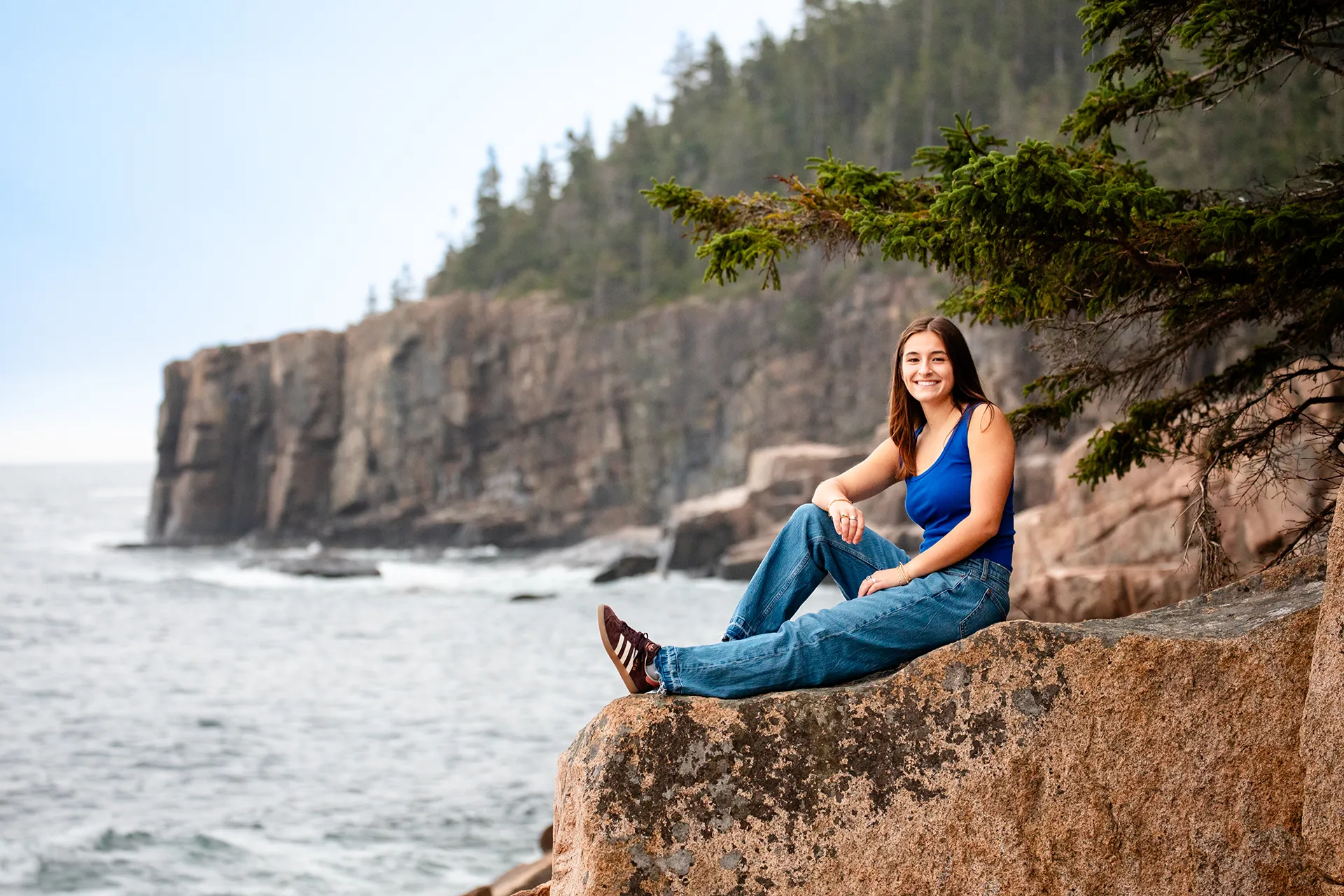 A girl poses on a rock during a high school senior portrait session near Otter Cliff in Acadia National Park, Maine.