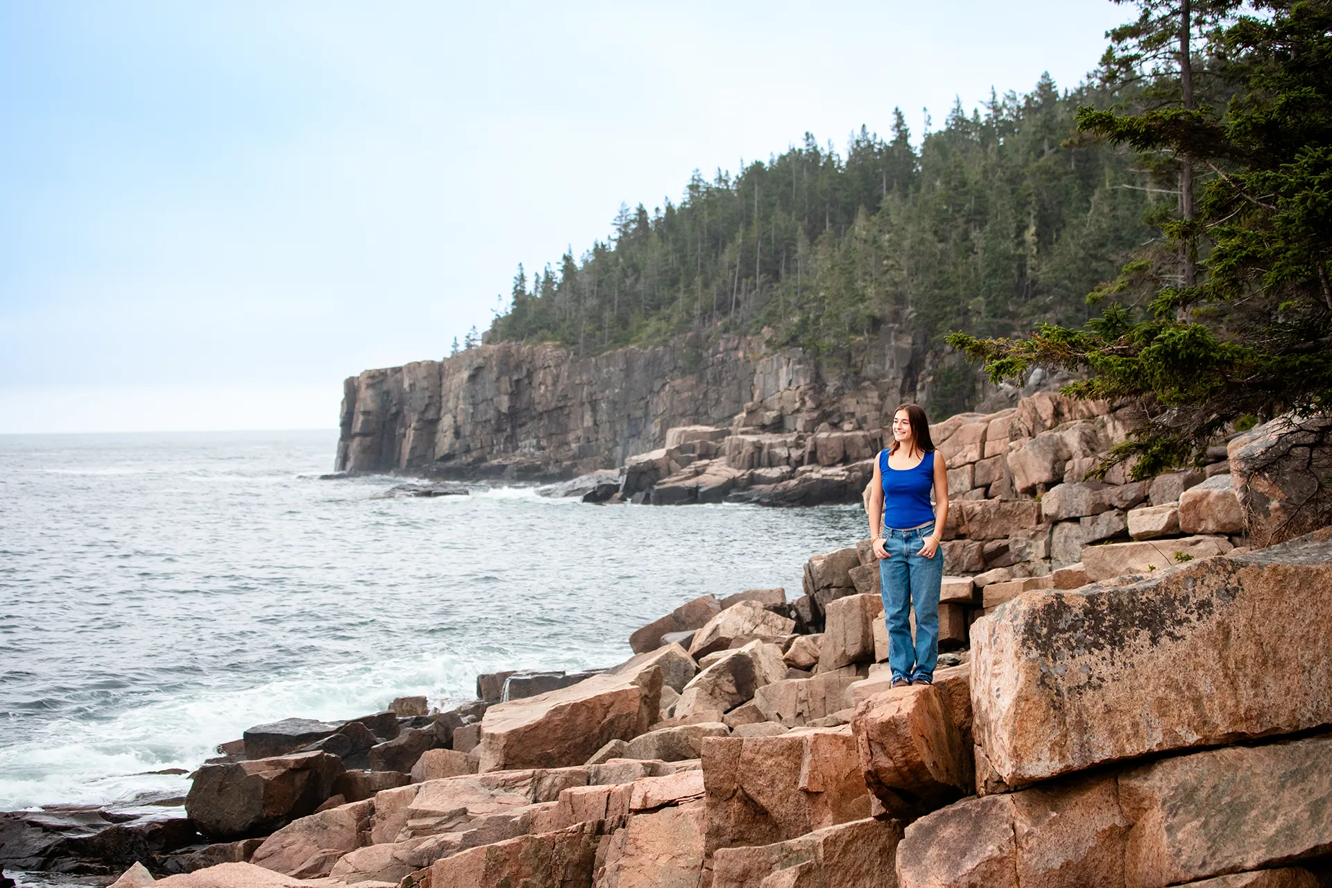 A high school senior poses on a rock during portrait session near the Ocean Path in Acadia National Park.