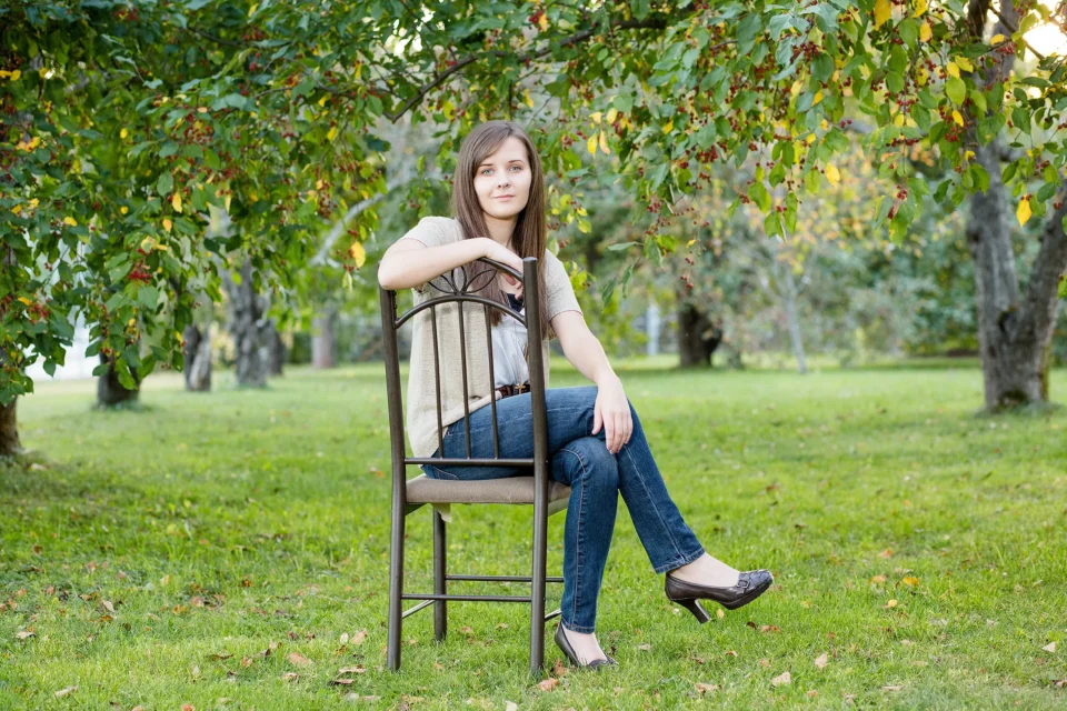 A girl sits and poses in an apple orchard during a senior portrait session in Littlefield Ornamental Garden at the University of Maine in Orono.