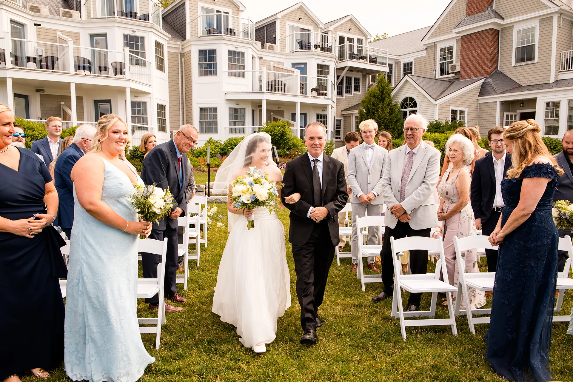 A bride and her dad smile at guests as they walk down the aisle during a wedding ceremony at the Bar Harbor Inn and Spa in Maine.