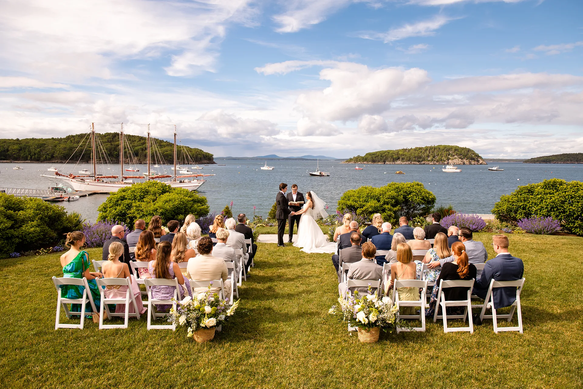 A bride and groom stand at the head of an aisle during a wedding ceremony overlooking Frenchman Bay at the Bar Harbor Inn and Spa in Maine.
