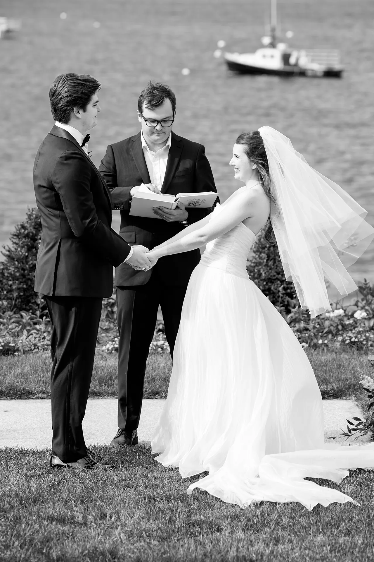 A bride and groom smile as they hold hands during a wedding ceremony at the Bar Harbor Inn and Spa in Maine.