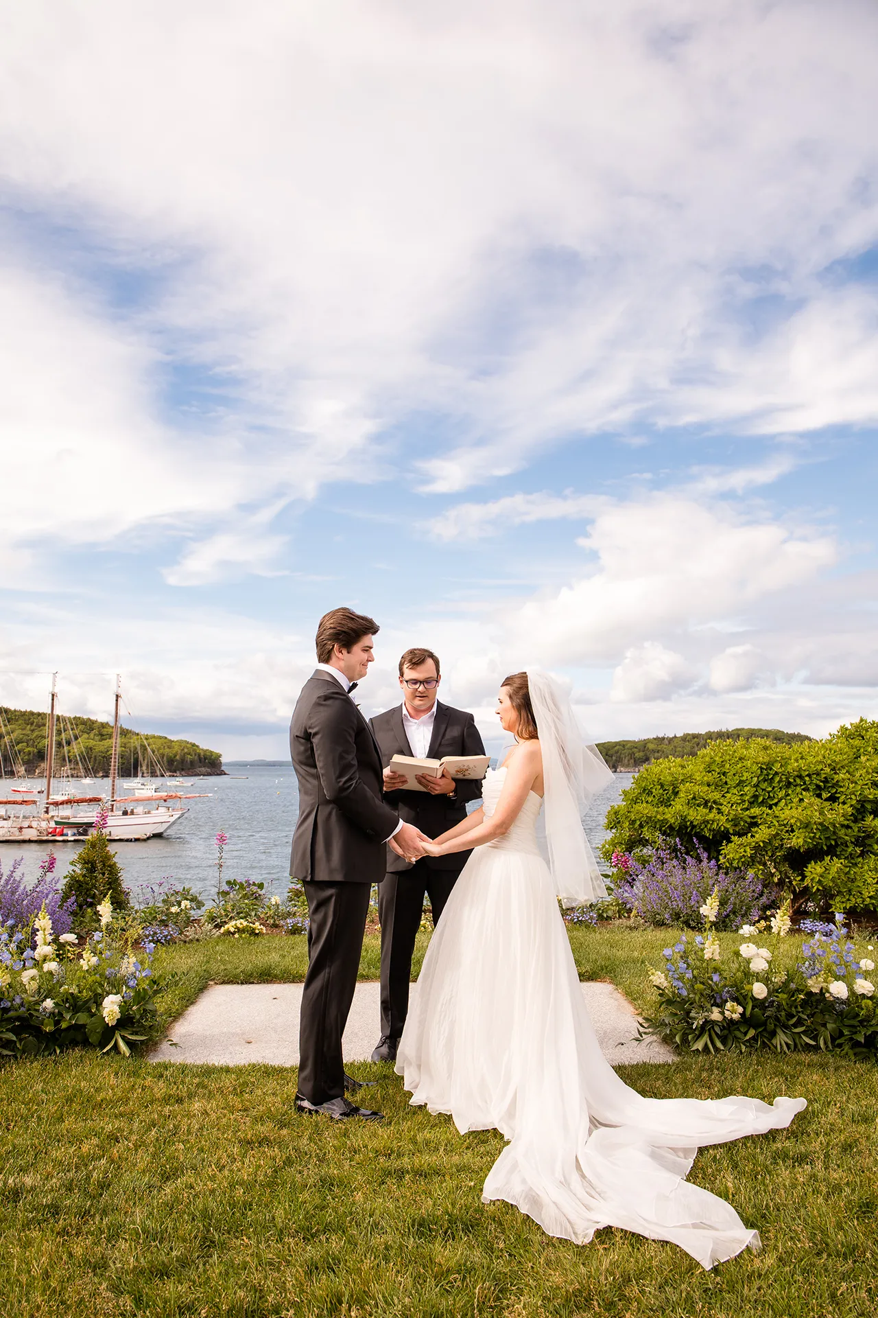 A bride and groom stand in front of Frenchman Bay a wedding ceremony at the Bar Harbor Inn and Spa near Acadia National Park in Maine.