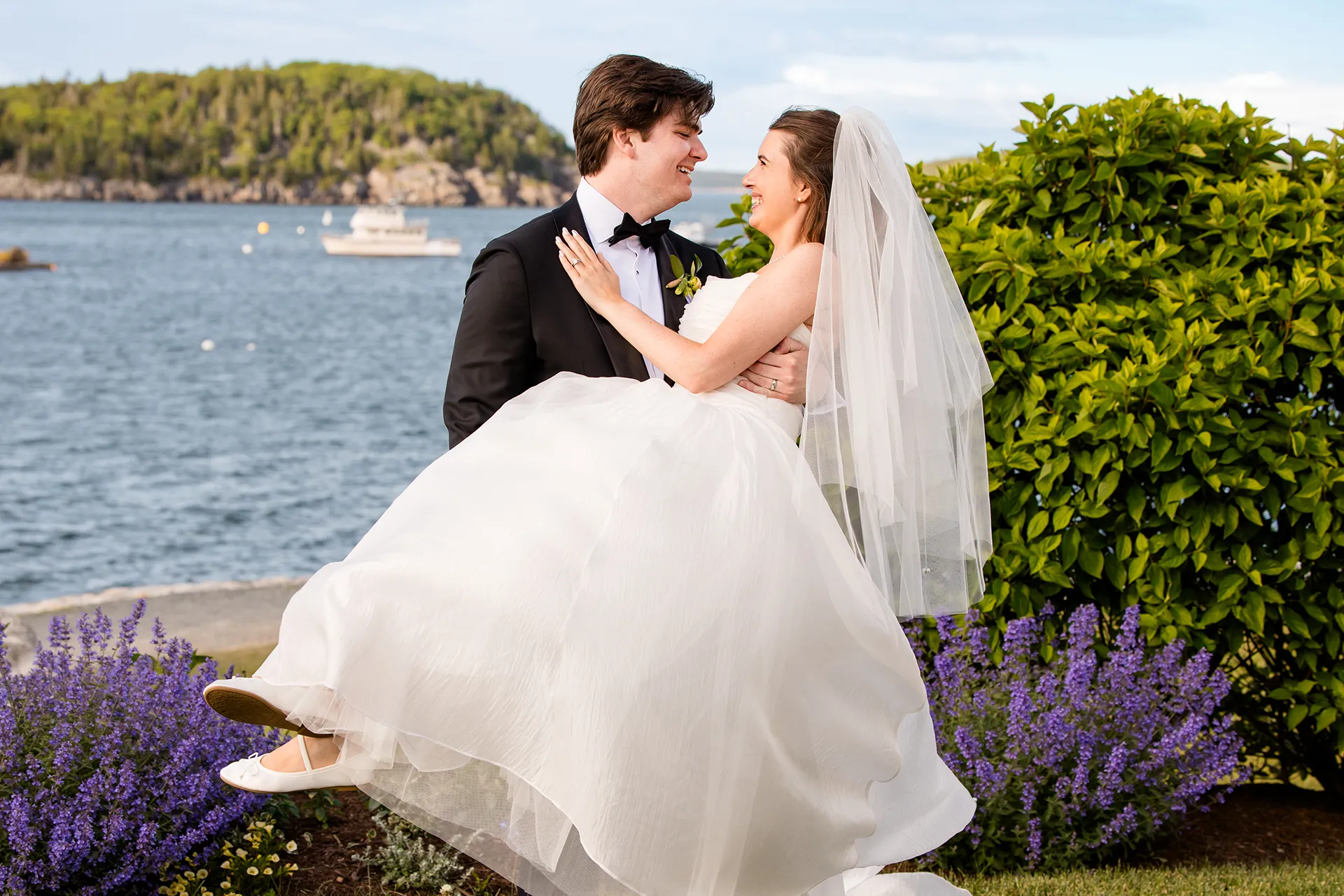 A groom picks up a bride and they laugh with each other during wedding portraits at the Bar Harbor Inn and Spa in Maine.