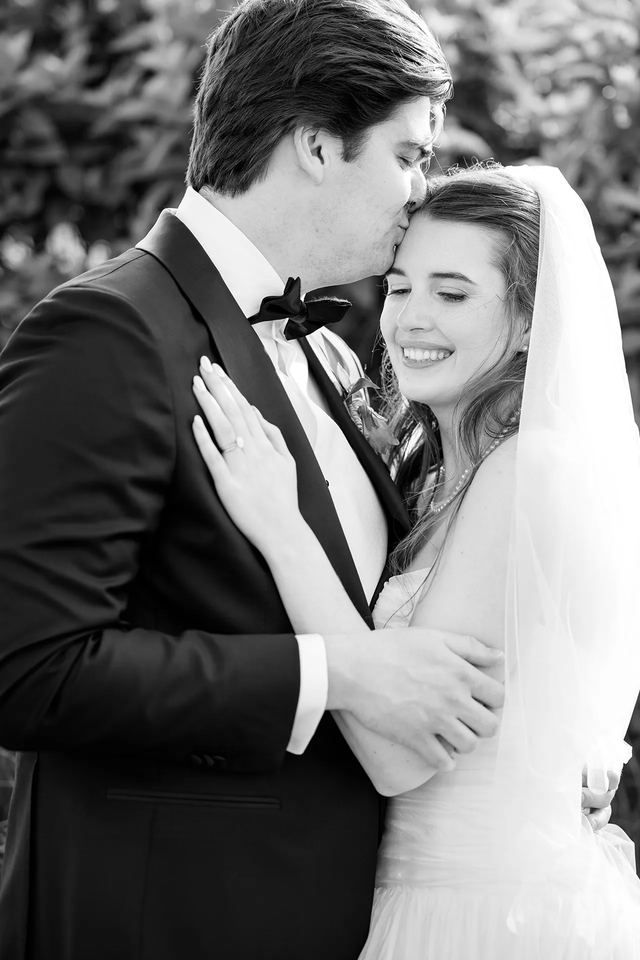 A bride smiles while a groom kisses her head at each other during wedding portraits at the Bar Harbor Inn and Spa near Acadia National Park in Maine.