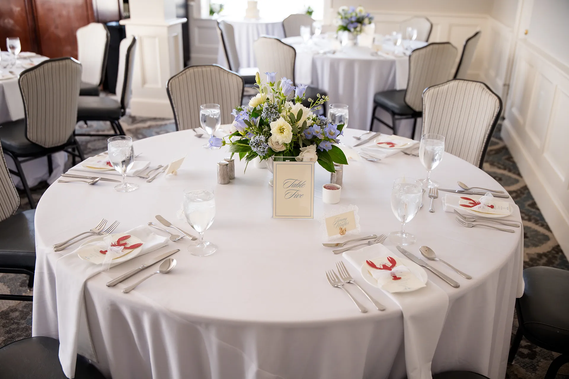 A closeup of a table with purple and while floral centerpieces for a wedding reception in the Porcupine Room at the Bar Harbor Inn and Spa in Maine.