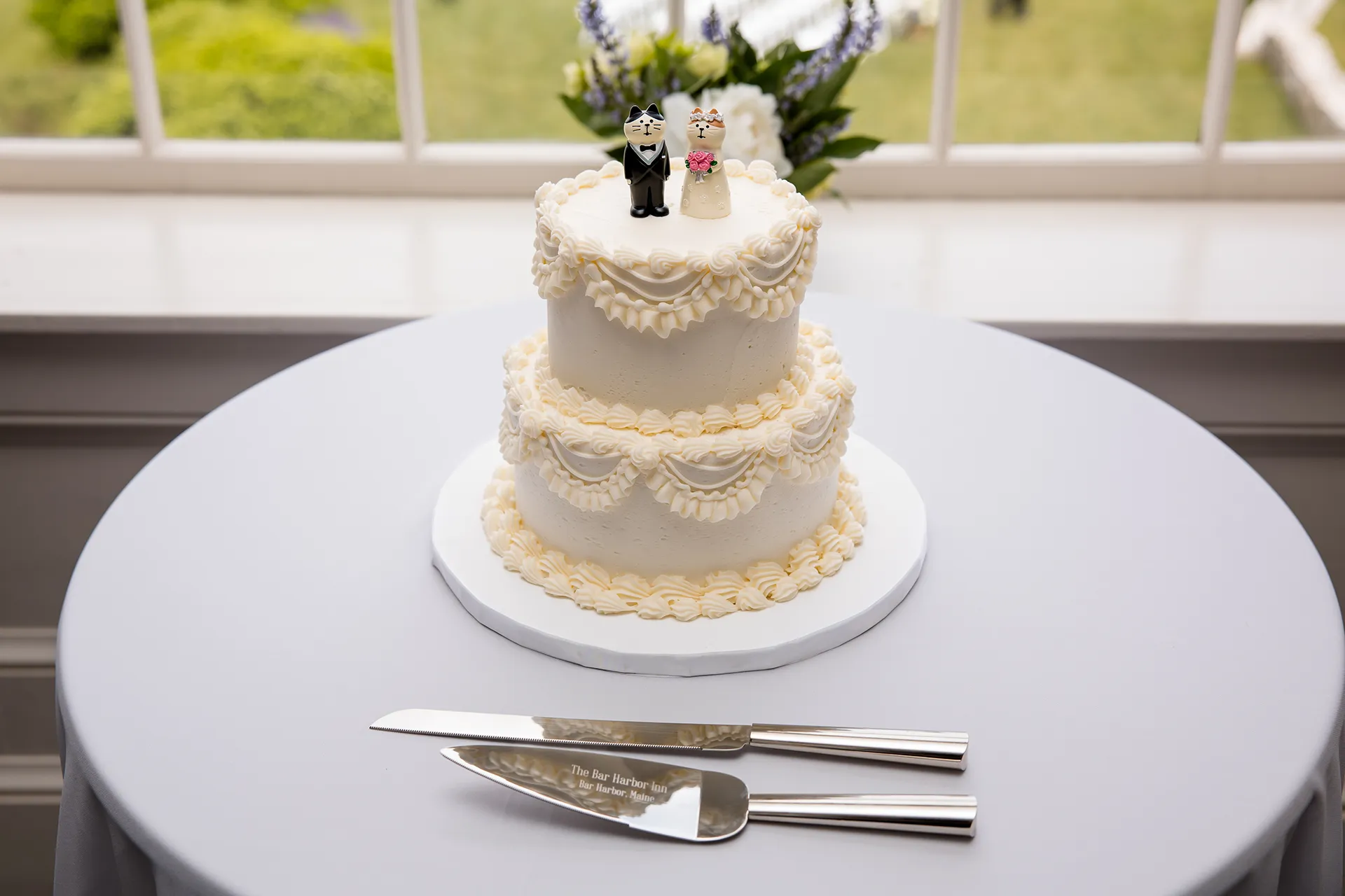 A closeup of a white wedding cake with bride and groom cat cake topper for a wedding reception at the Bar Harbor Inn and Spa in Maine.