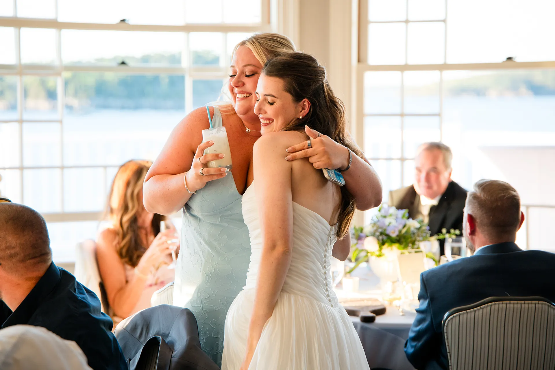 A bride hugs a bridesmaid during a wedding reception in the Porcupine Room at the Bar Harbor Inn and Spa in Maine.