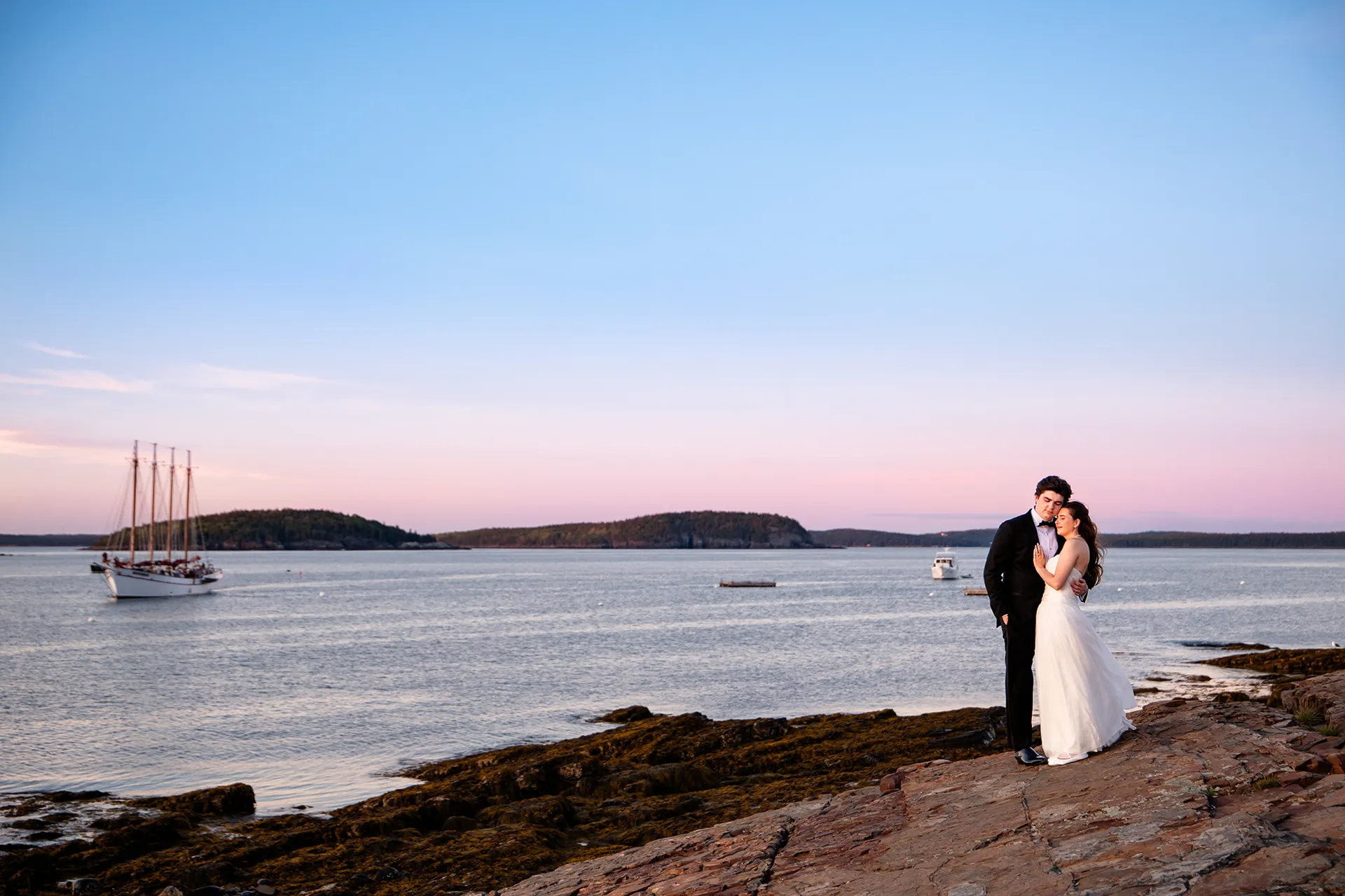 A bride and groom snuggle together on a cliff overlooking Frenchman Bay as a boat comes in at the Bar Harbor Inn and Spa in Maine.