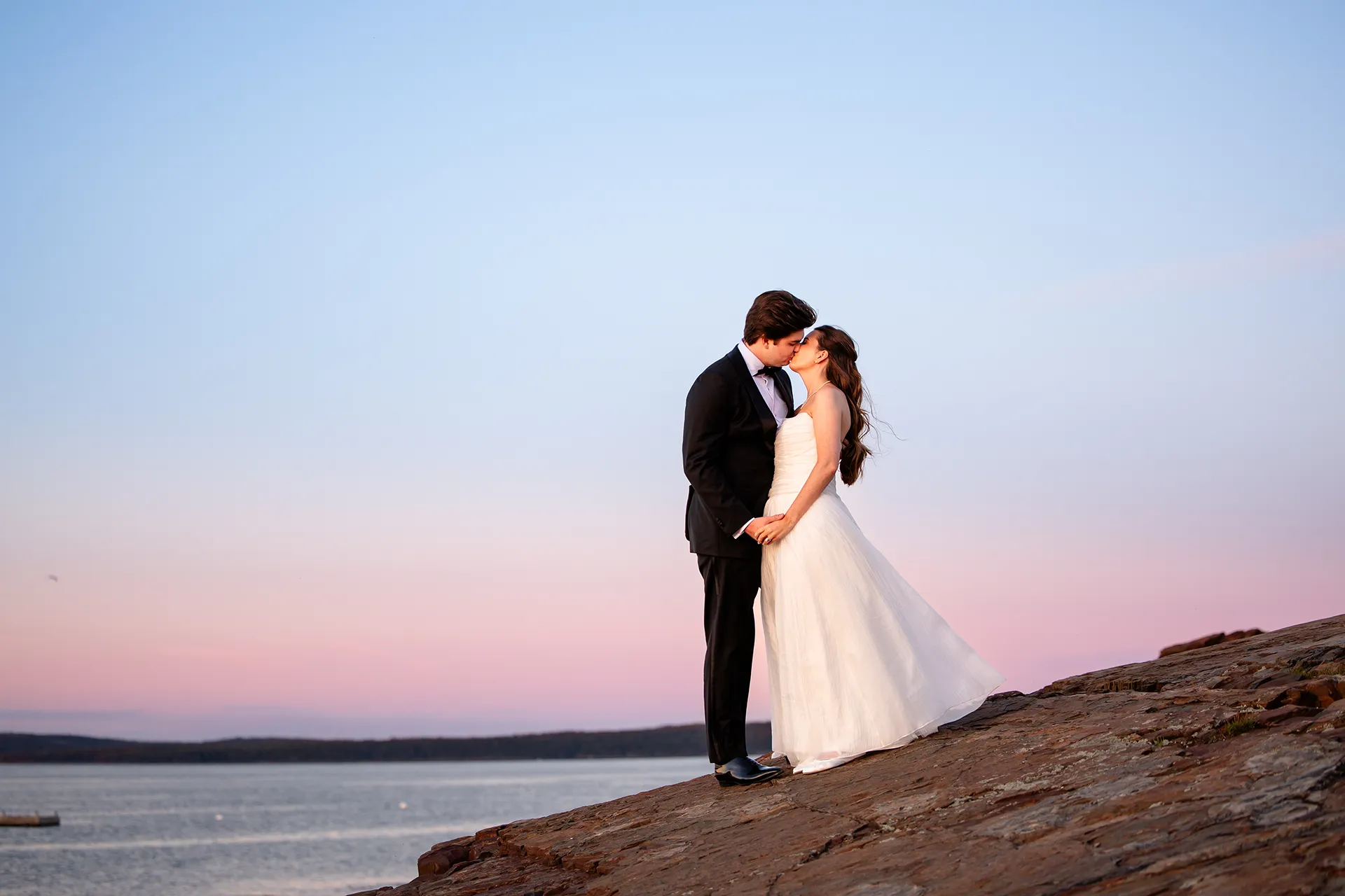 A newly married couple kiss while standing on a cliff during their wedding portraits at the Bar Harbor Inn and Spa in Maine.