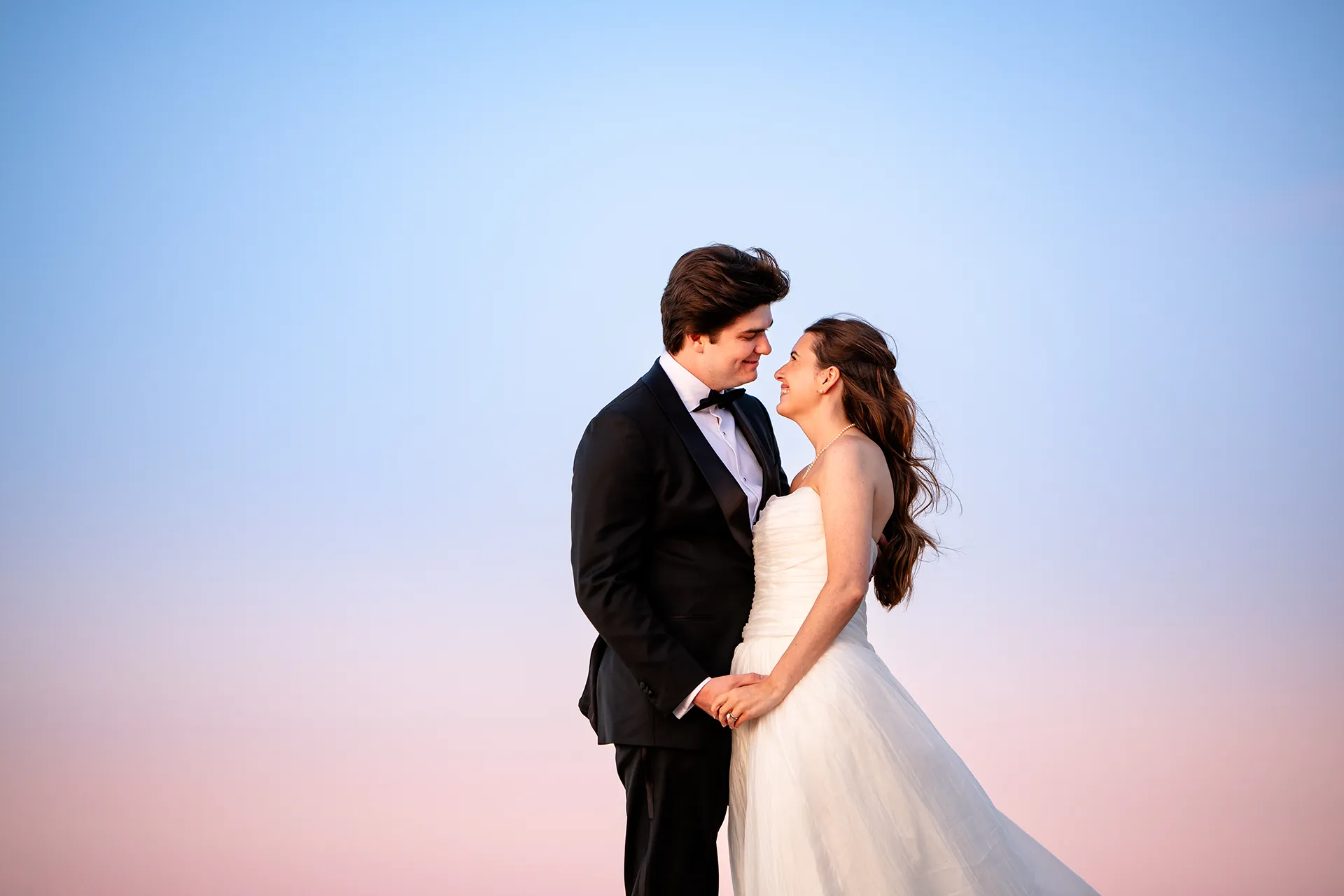 A bride and groom smile at each other during sunset wedding portraits at the Bar Harbor Inn and Spa in Maine.