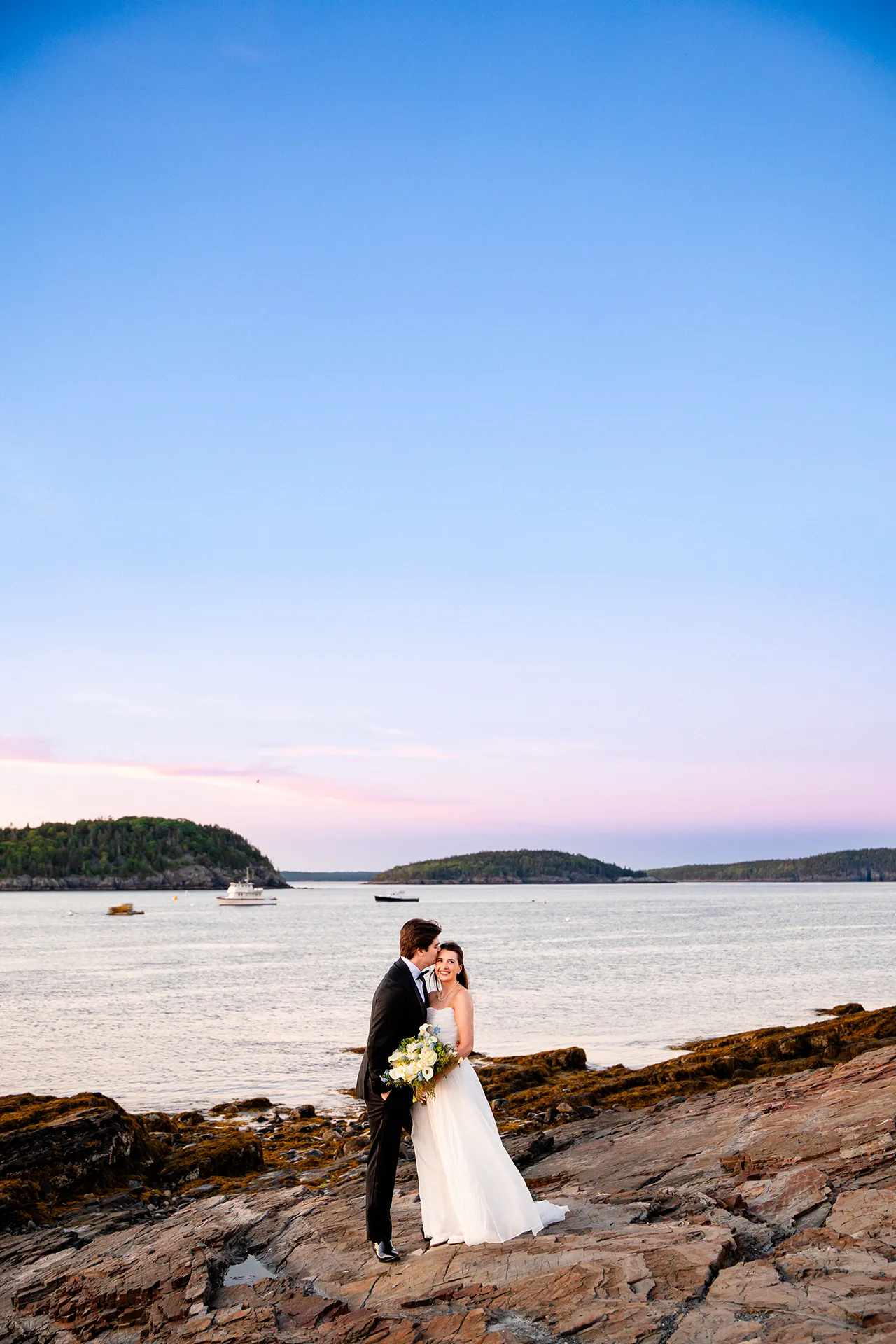 A groom kisses a bride on the head during their sunset wedding portraits at the Bar Harbor Inn and Spa near Acadia National Park in Maine.