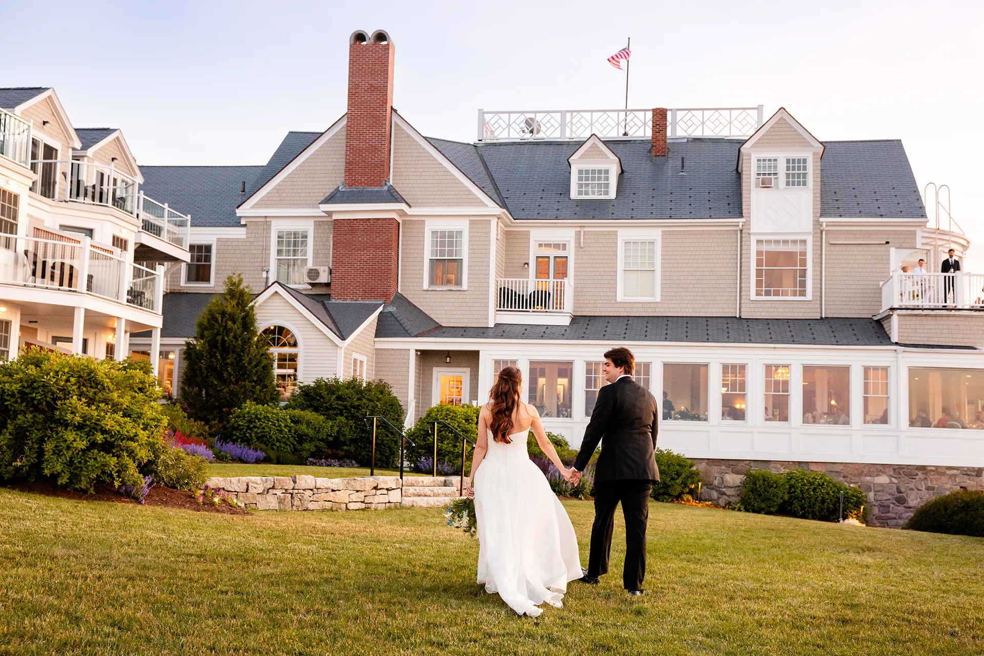 A newly married couple hold hands as they walk towards the Bar Harbor Inn and Spa during their wedding portraits in Bar Harbor, Maine.
