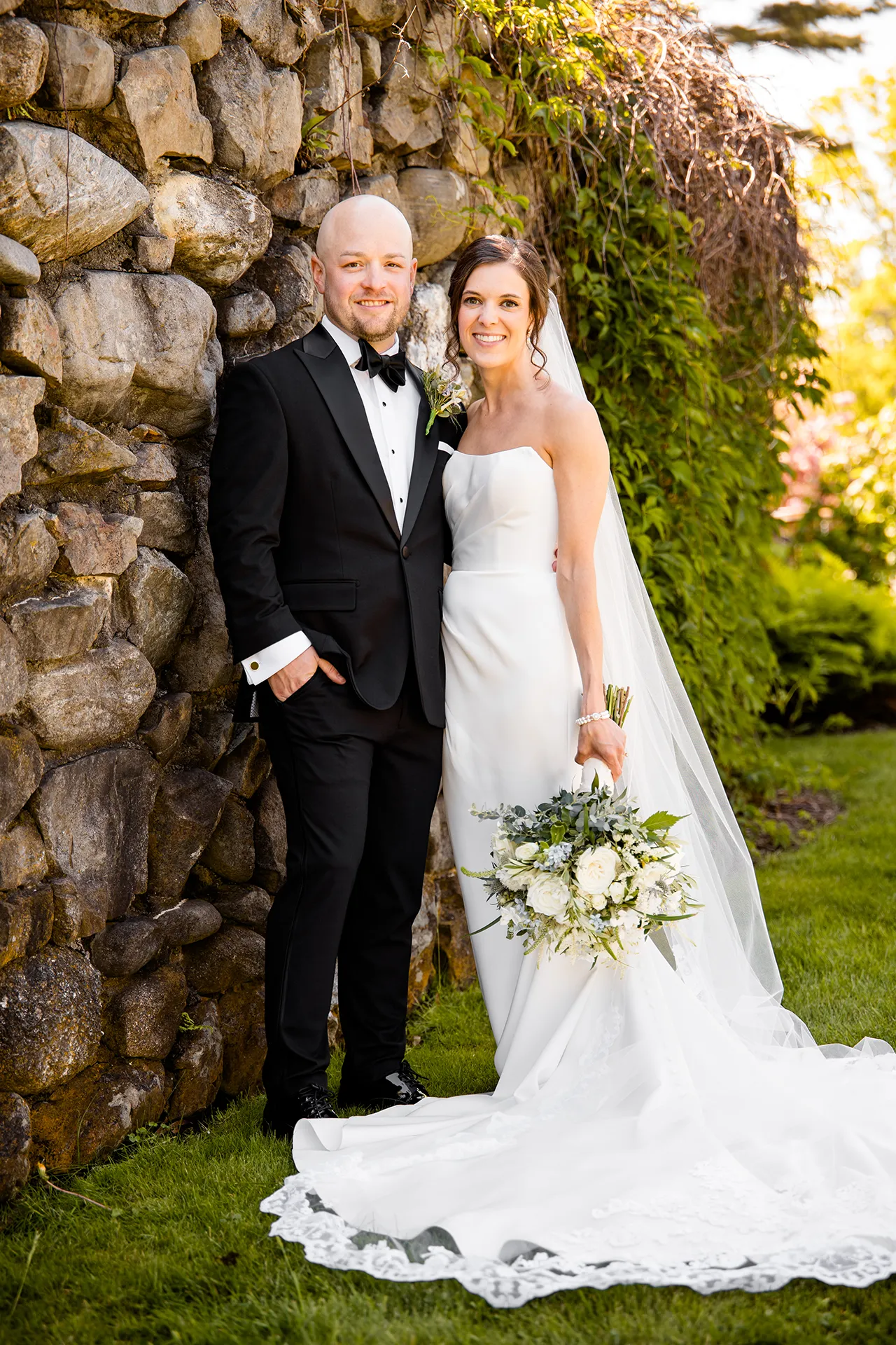 A bride and groom smile as they pose for wedding portraits in a garden at the Atlantic Oceanside Hotel & Event Center in Bar Harbor, Maine.