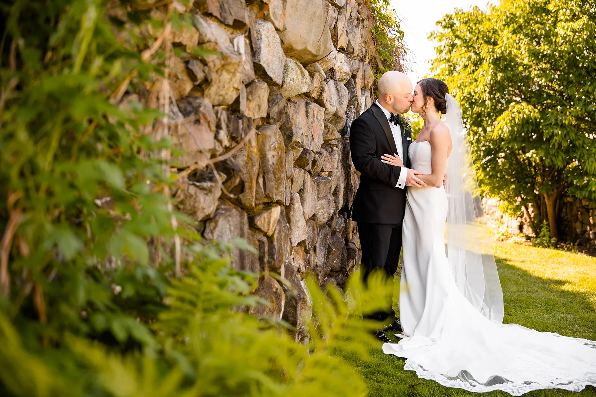A bride and groom kiss in the Willow's garden during wedding portraits at the Atlantic Oceanside Hotel & Event Center in Bar Harbor, Maine.