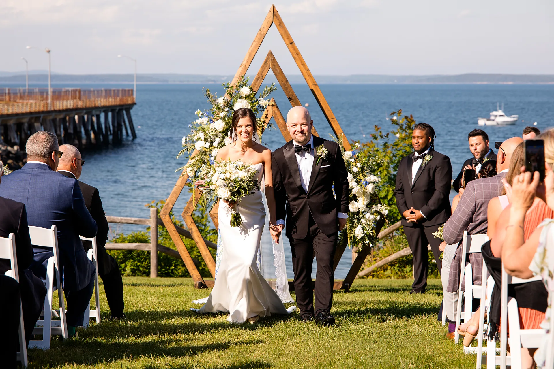 A bride and groom hold hands as they walk down the aisle during a wedding ceremony at the Atlantic Oceanside Hotel & Event Center in Bar Harbor.