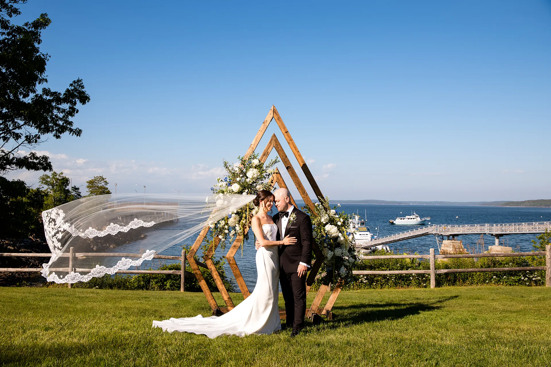 A bride and groom rest their heads together while the bride's veil flies in the breeze at the Atlantic Oceanside Hotel & Event Center in Bar Harbor, Maine.
